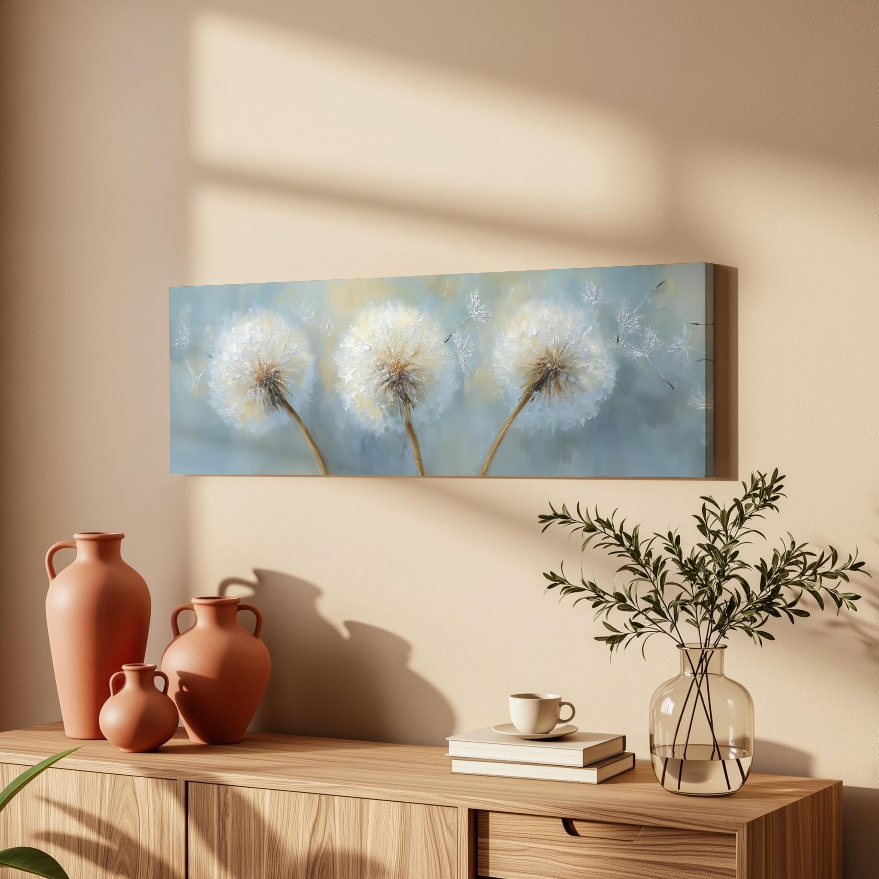 a wooden cabinet with a painting of dandelions hanging on the wall above it. The cabinet also has three orange vases, a glass vase with greenery, and a stack of books on top.