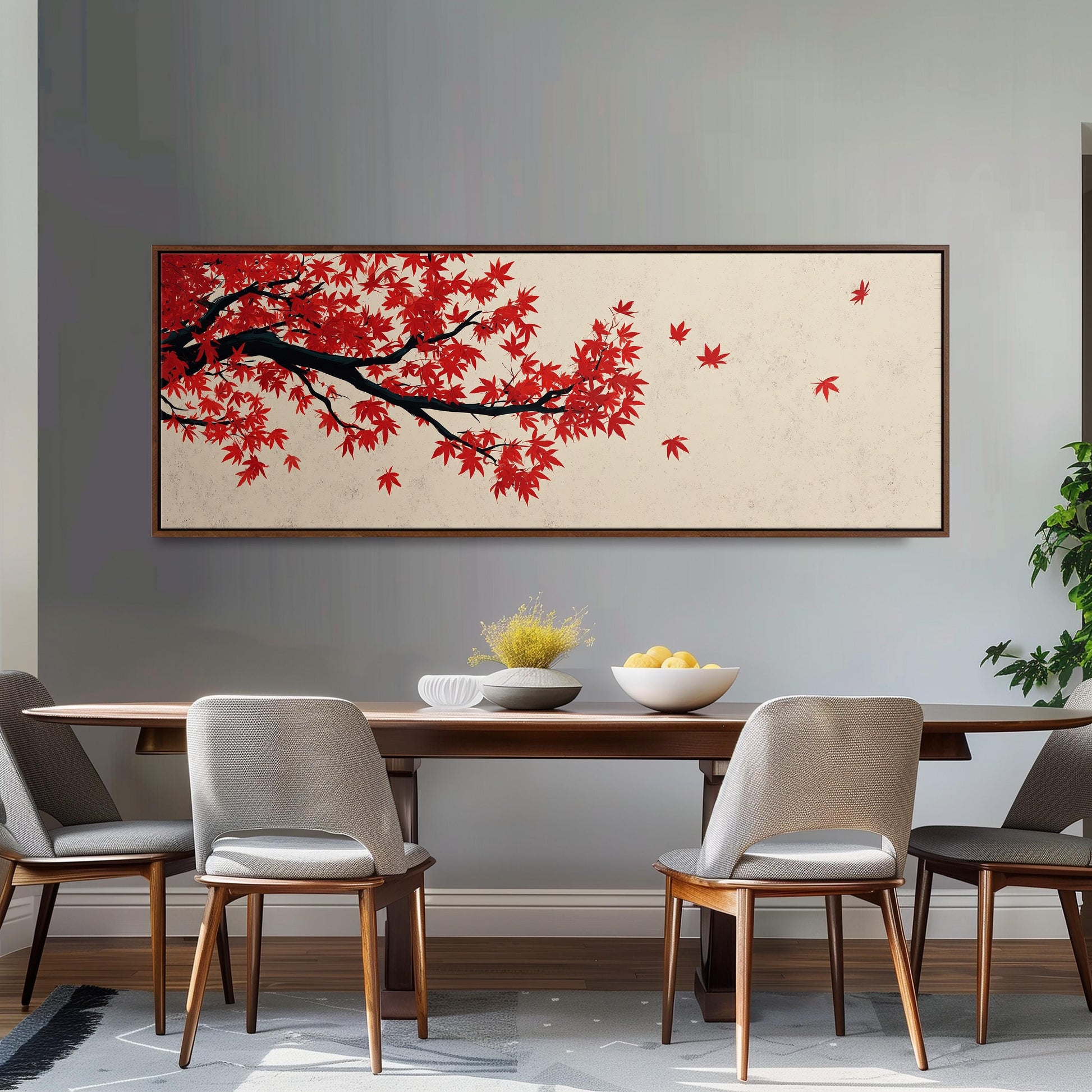 a dining room with a wooden table and four chairs. Above the table, there is a large painting depicting a tree with red leaves. The painting is framed and hangs on the wall. The table is set with a bowl of fruit and a vase of flowers, creating a cozy and inviting atmosphere.