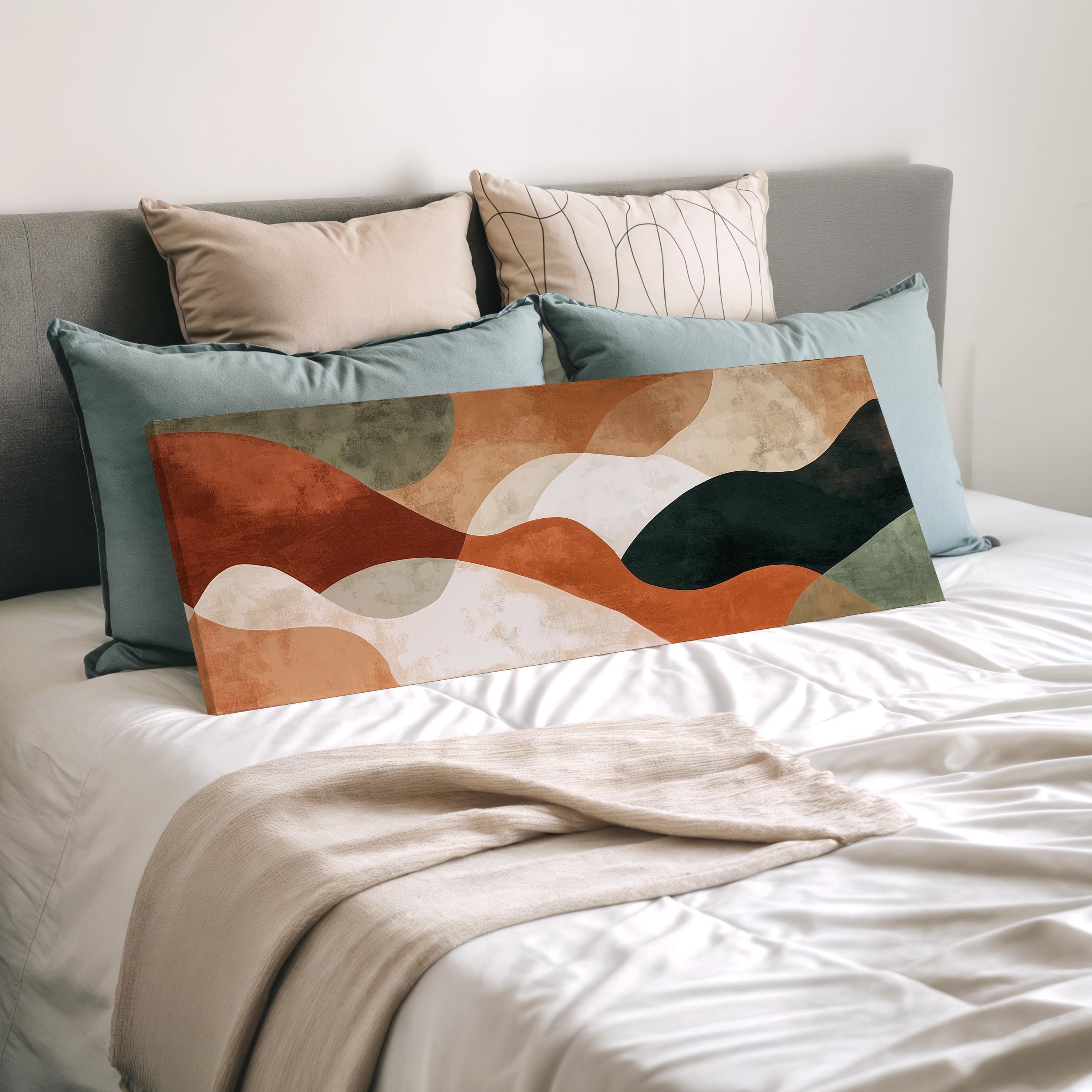 a bed with a white comforter and a large abstract painting or artwork placed on it. The bed is surrounded by multiple pillows, creating a cozy and inviting atmosphere.