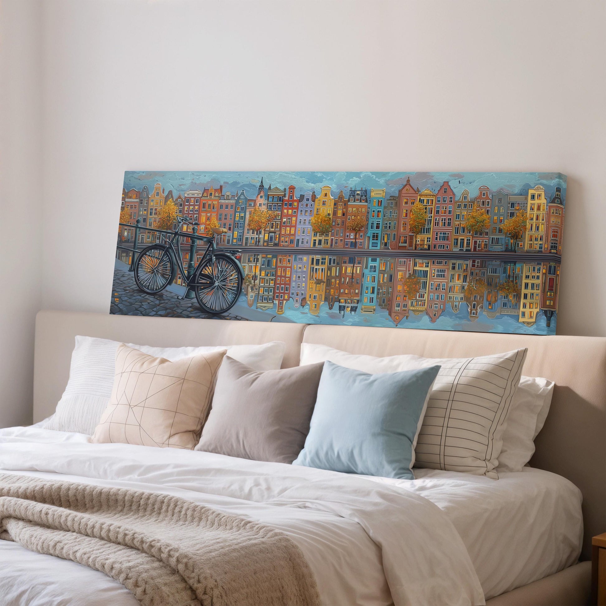 a large painting of a cityscape with a bicycle in the foreground, hanging on a wall above a bed with white pillows and a gray blanket.
