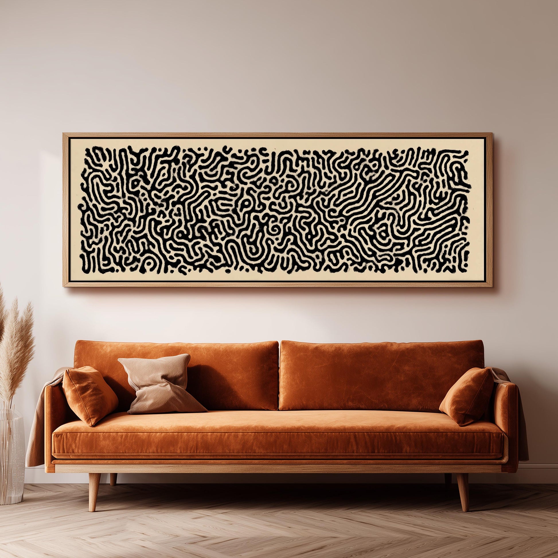 a large, abstract black and white artwork hanging on a white wall above a brown sofa with two pillows.