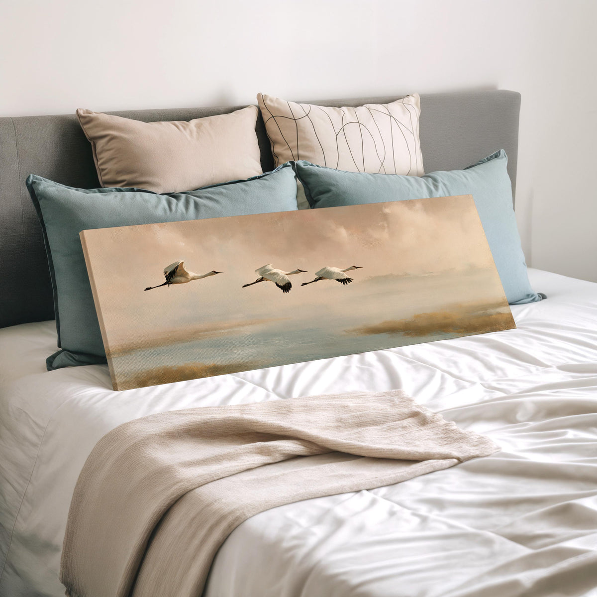 Cranes flying over a calm shore at dusk wide panoramic canvas print laid on a bed to show its size