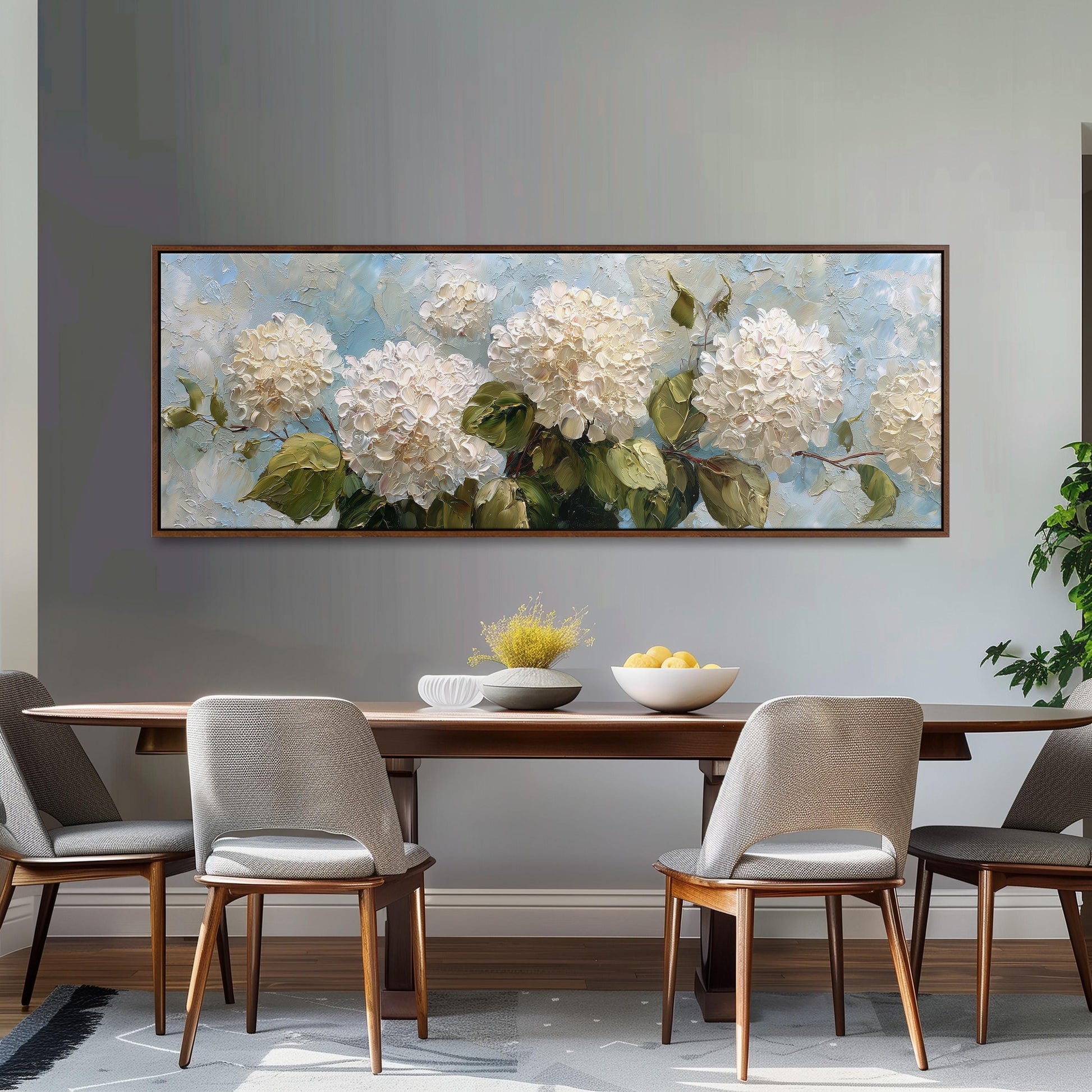 a dining room with a large painting of white hydrangeas hanging on the wall above a wooden dining table with four chairs. The table is set with a bowl of fruit and a vase of flowers, creating a cozy and inviting atmosphere.