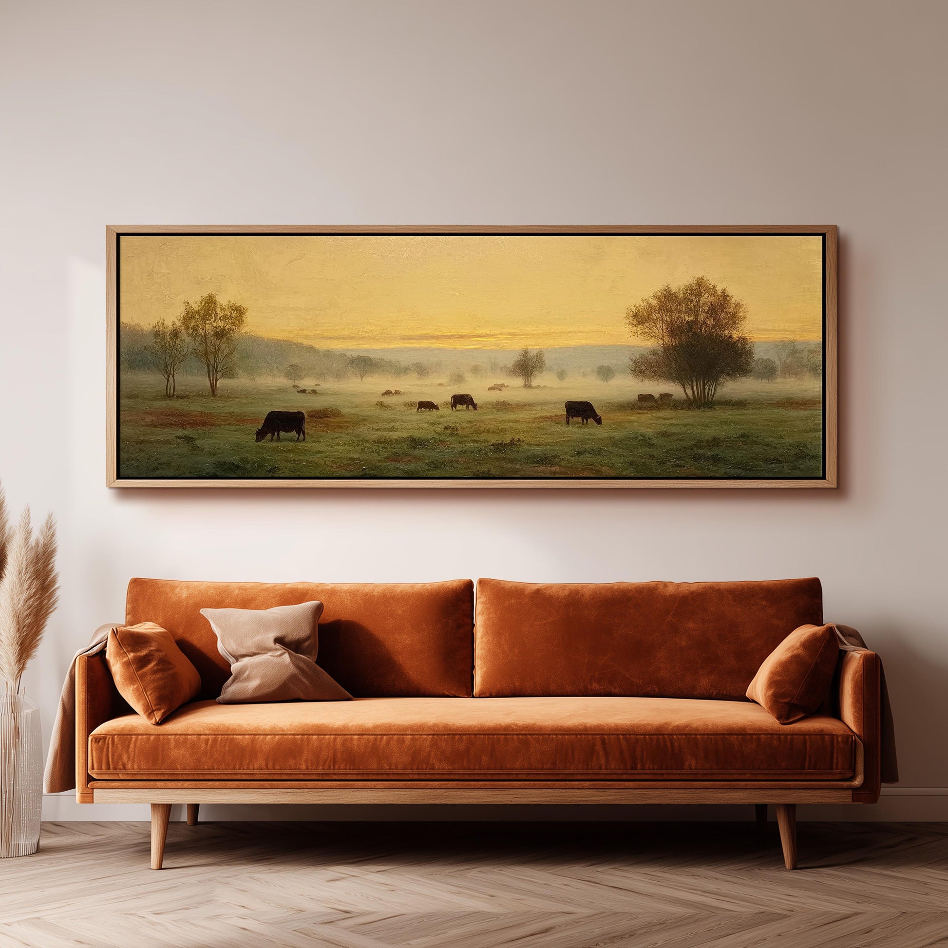 a large painting of a pastoral scene with cows grazing in a field, hanging on a wall above a brown sofa.