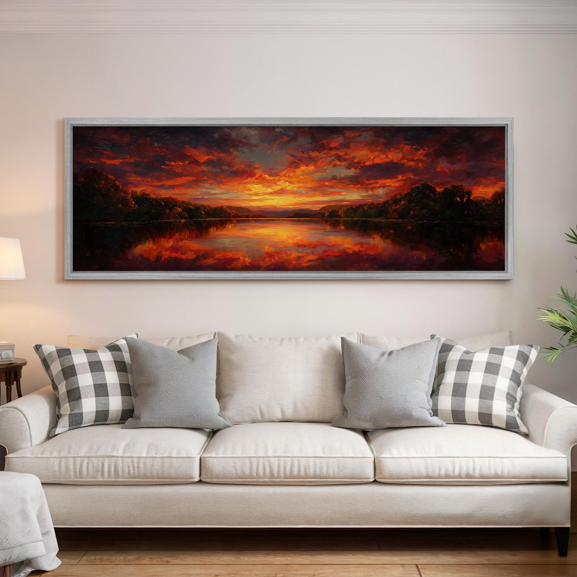 a large, framed painting of a sunset landscape hanging on a wall above a white couch with gray and white patterned pillows.