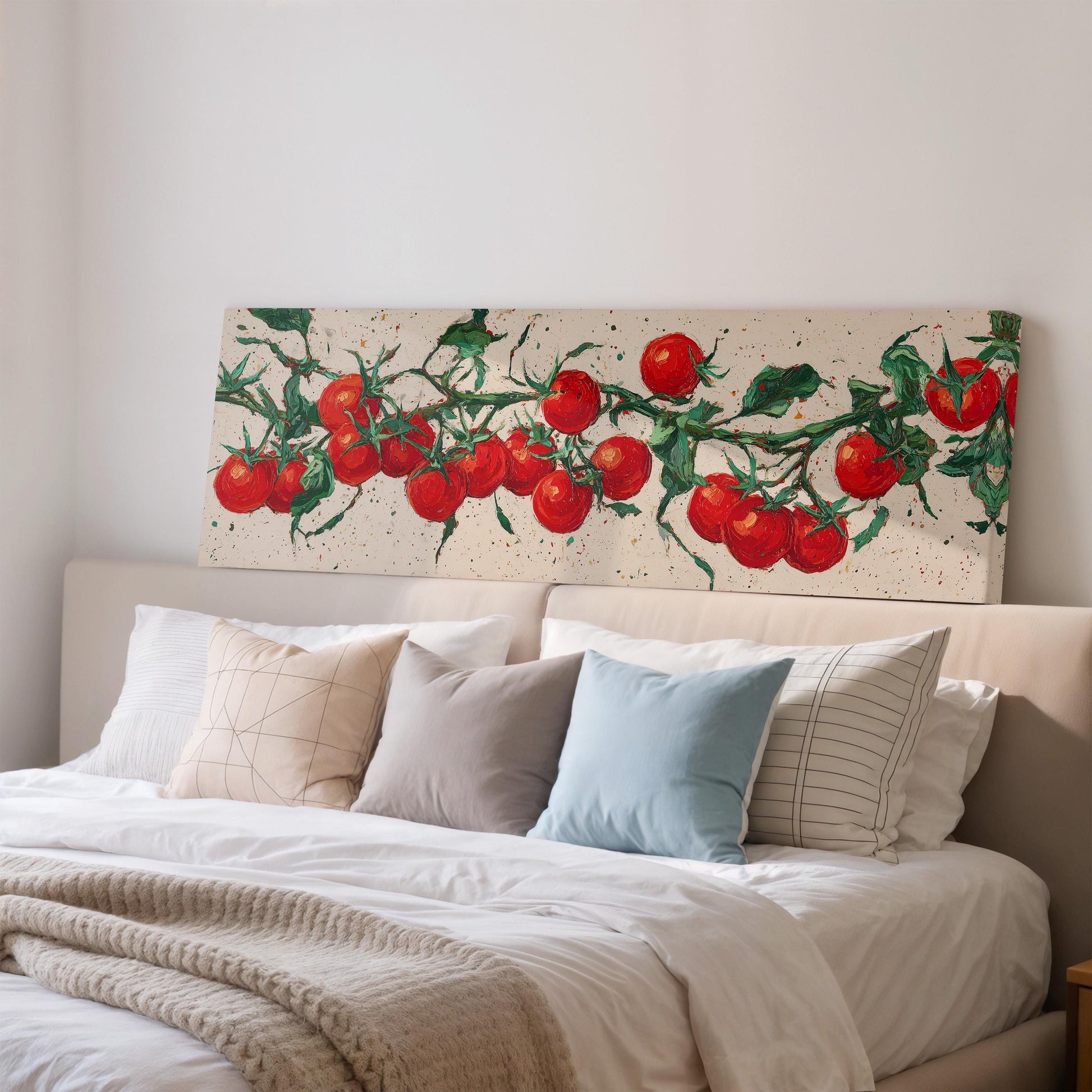 a large bed with a white comforter and a variety of pillows, including a blue pillow and a striped pillow. Above the bed, there is a large canvas print depicting a branch of red tomatoes.