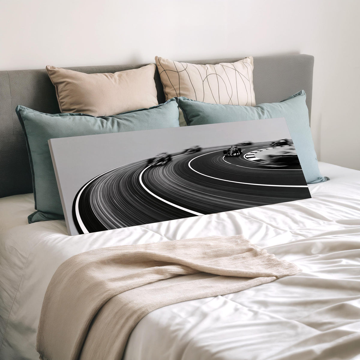 Race cars sweeping around a curve in black and white wide panoramic canvas print laid on a bed to show its size