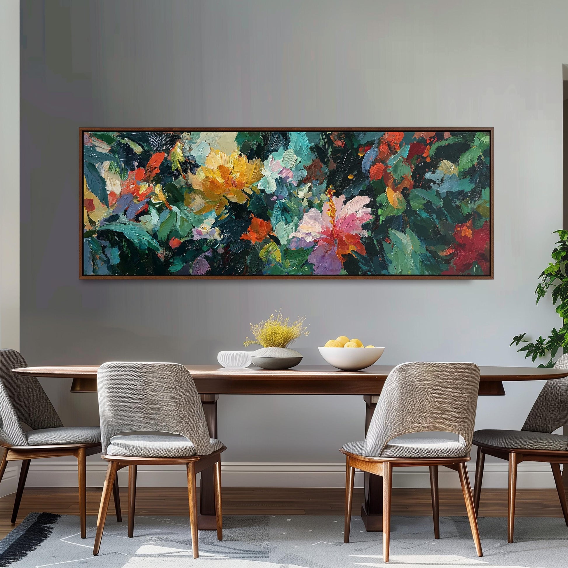a dining room with a large, colorful painting hanging on the wall above a wooden dining table. The table is set with a bowl of fruit and a vase of flowers, creating a welcoming and vibrant atmosphere. The room is furnished with four chairs, two on each side of the table, and a potted plant is visible in the background.