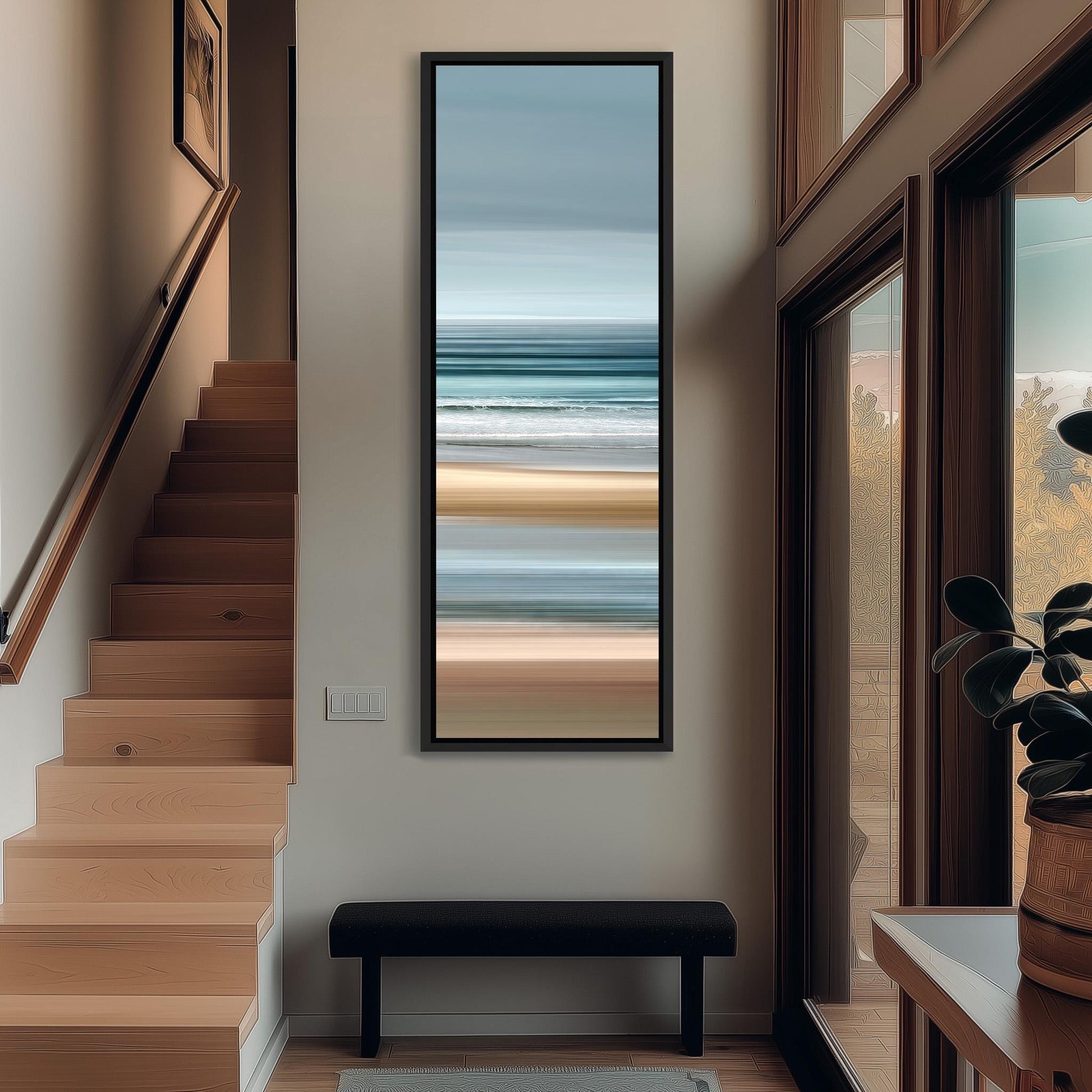 a hallway with a large window, a wooden staircase, and a framed painting of a beach scene hanging on the wall.