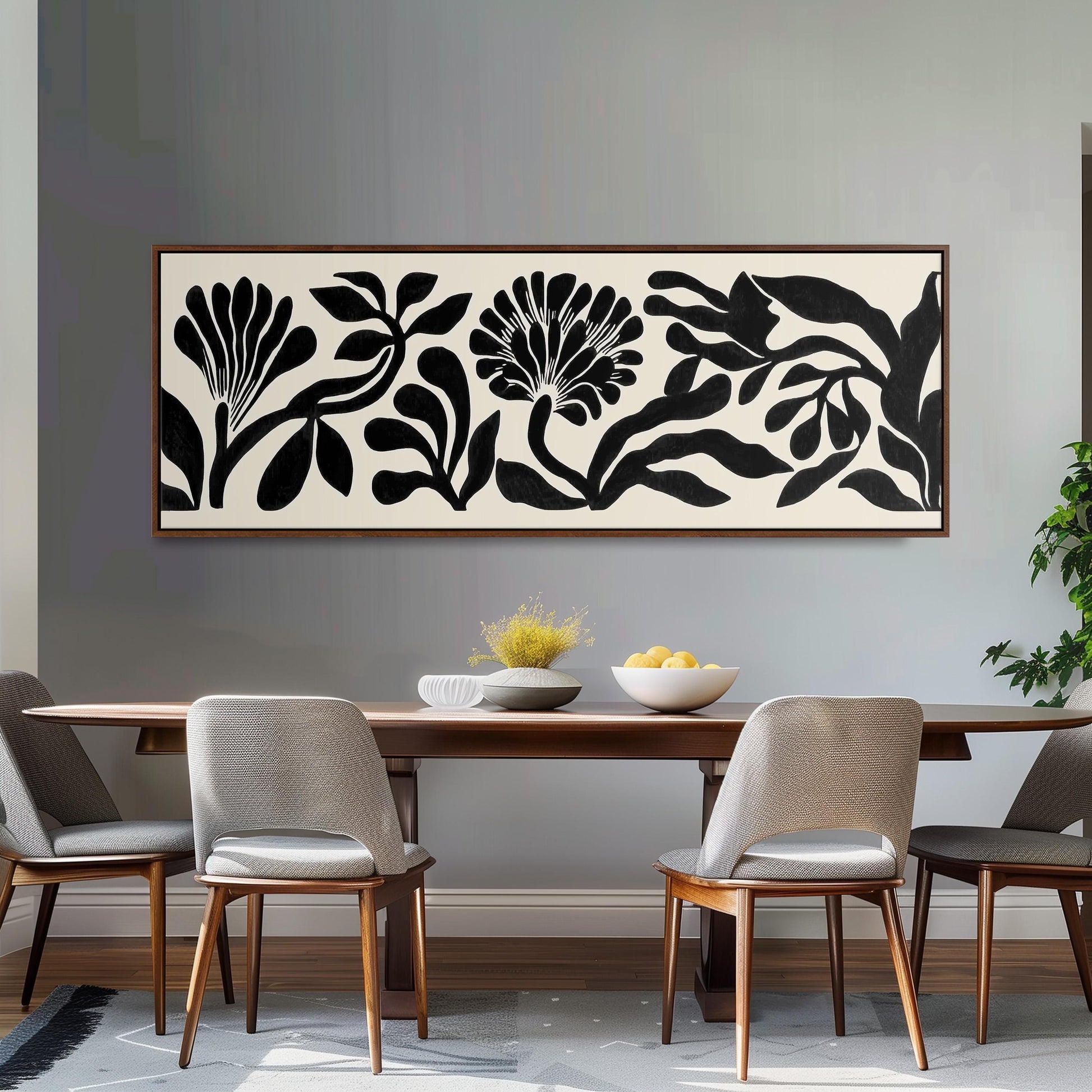 a dining room with a wooden table and four chairs. Above the table, there is a large black and white abstract painting depicting stylized flowers and leaves. The table is set with a bowl of fruit and a vase of flowers, creating a cozy and inviting atmosphere.