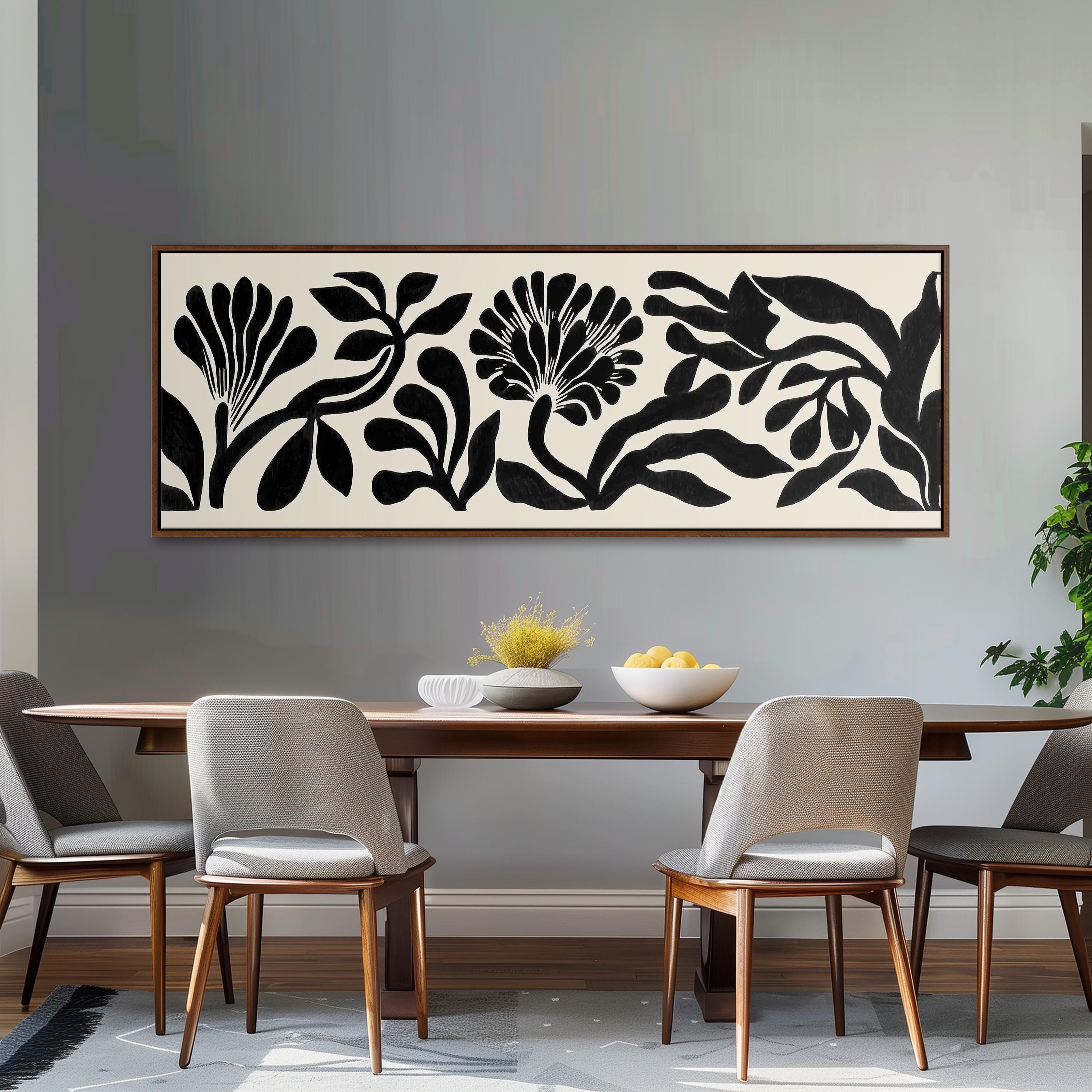 a dining room with a wooden table and four chairs. Above the table, there is a large black and white abstract painting depicting stylized flowers and leaves. The table is set with a bowl of fruit and a vase of flowers, creating a cozy and inviting atmosphere.