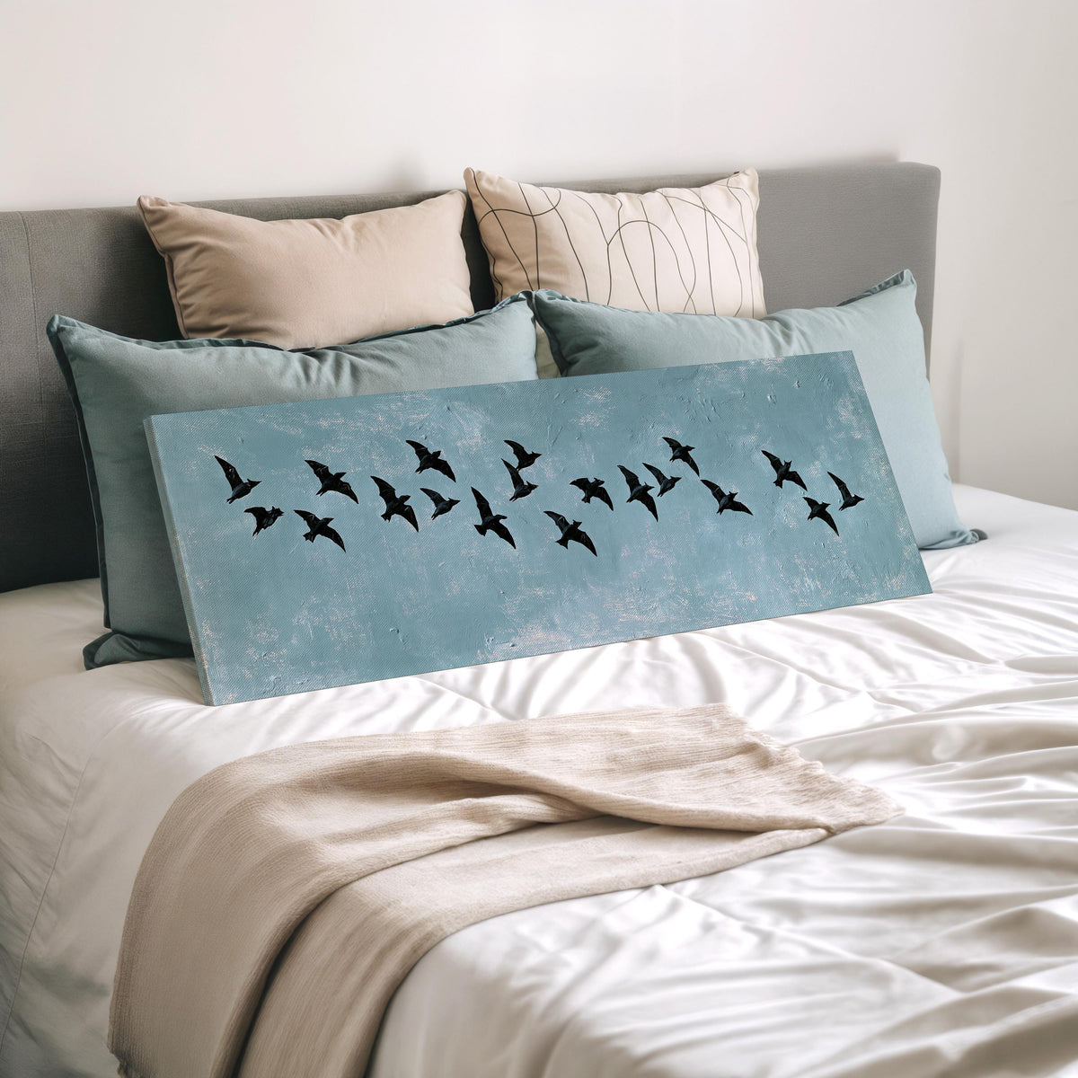 Flock of black birds on a teal sky wide panoramic canvas print laid on a bed to show its size