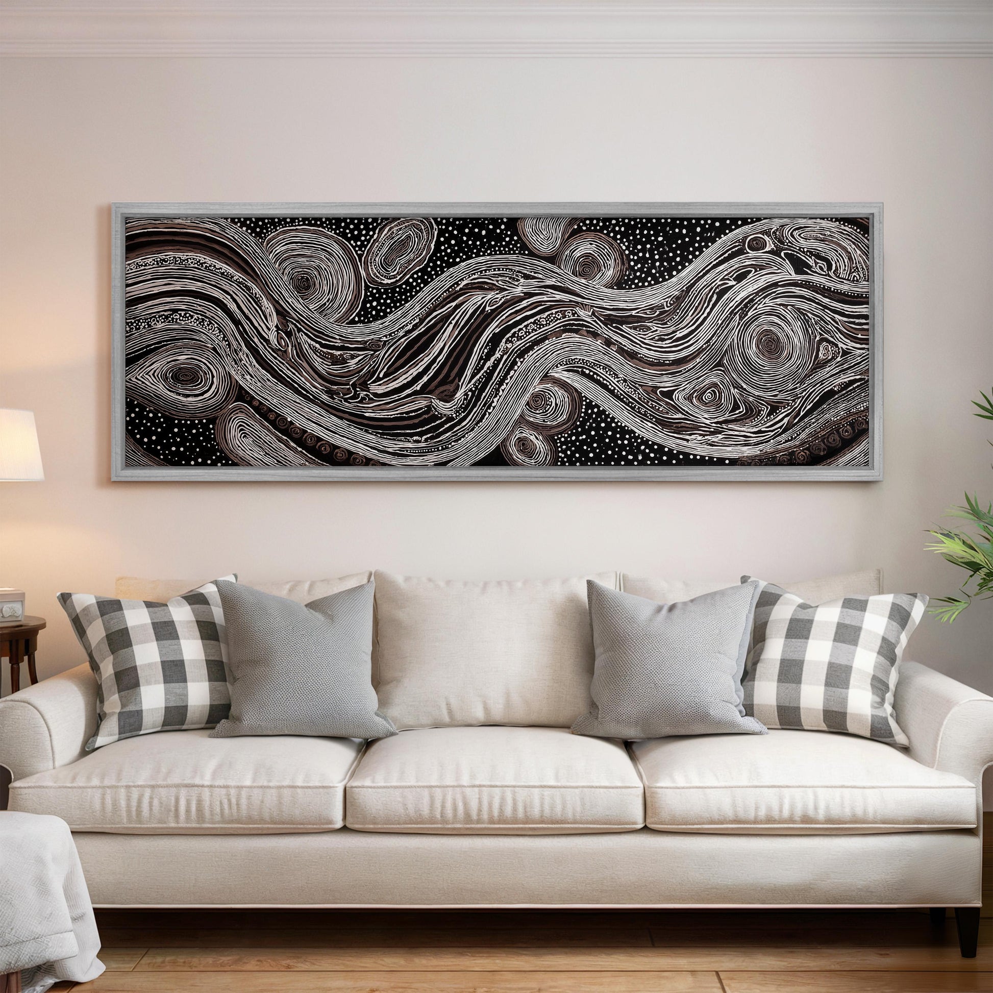a large, abstract painting hanging on a wall above a white couch with gray and white plaid throw pillows.