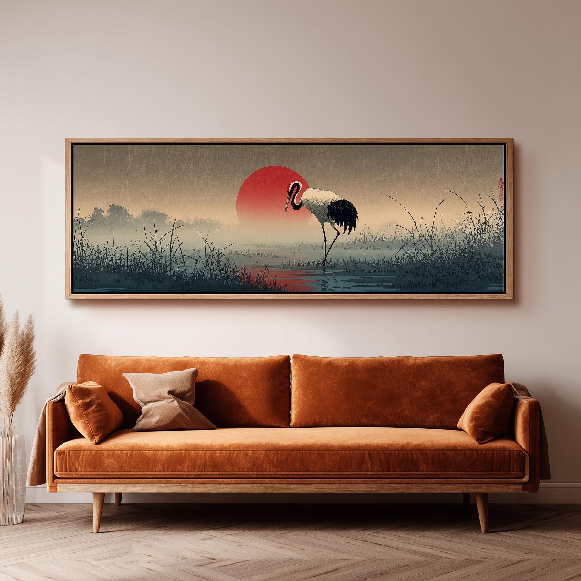 a large, framed painting of a crane standing in a field with a red sun in the background.