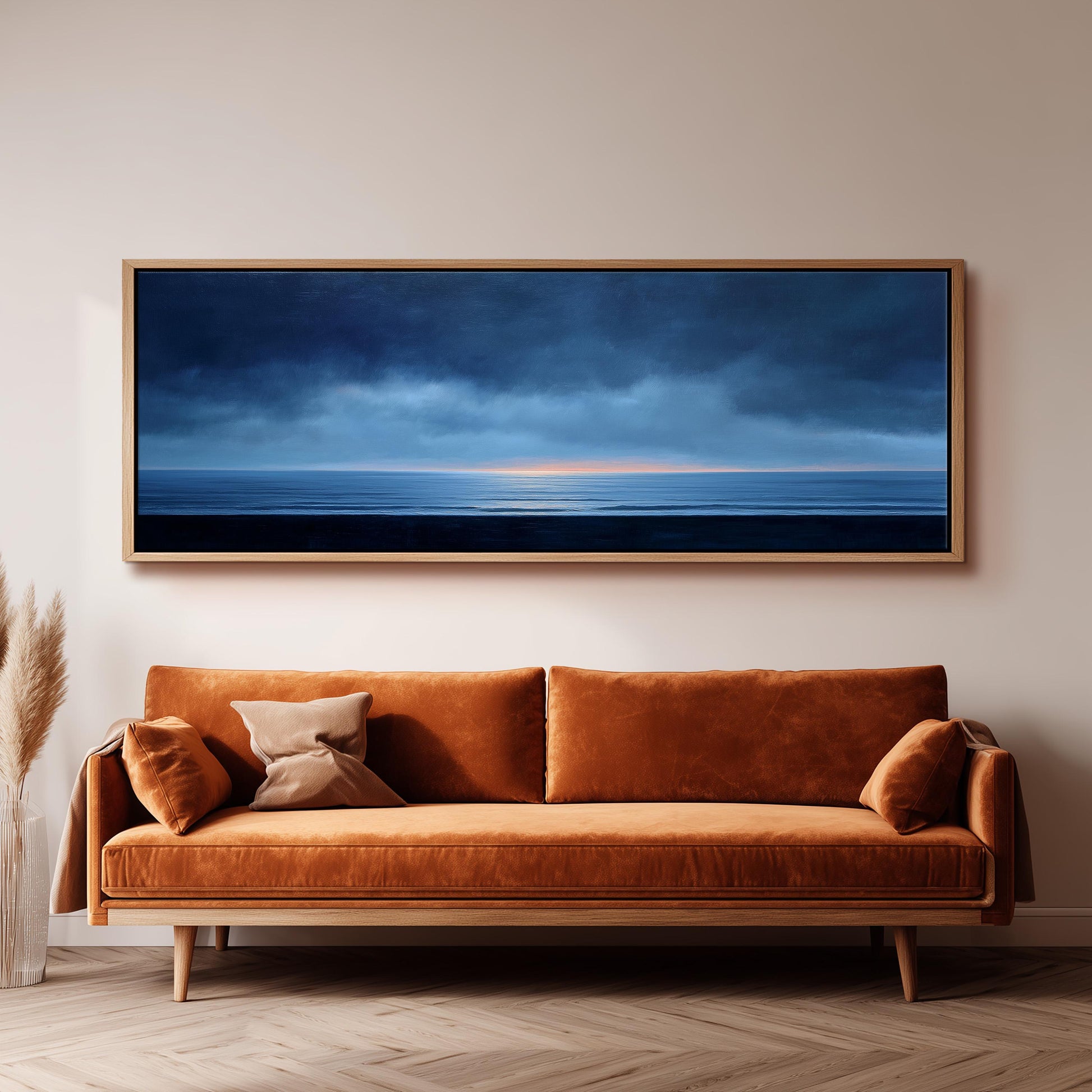 a large, rectangular painting of a serene ocean scene hanging on a wall above a brown sofa with orange cushions.