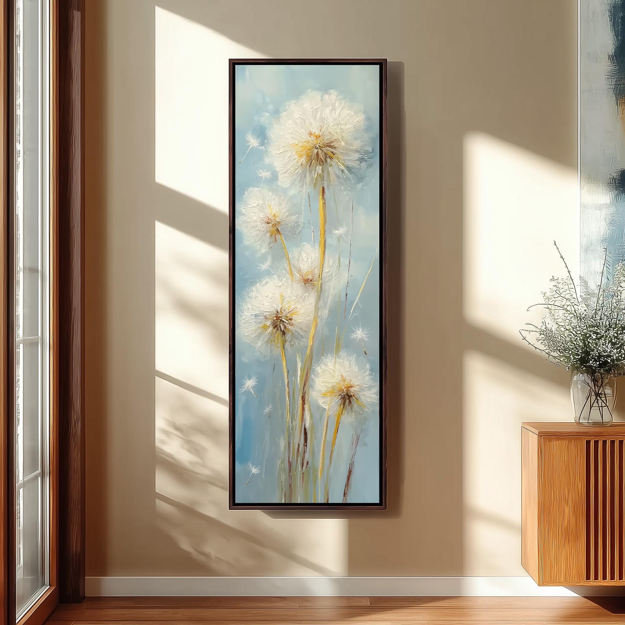 a large framed painting of dandelions hanging on a wall in a room with a wooden cabinet and a vase of flowers.