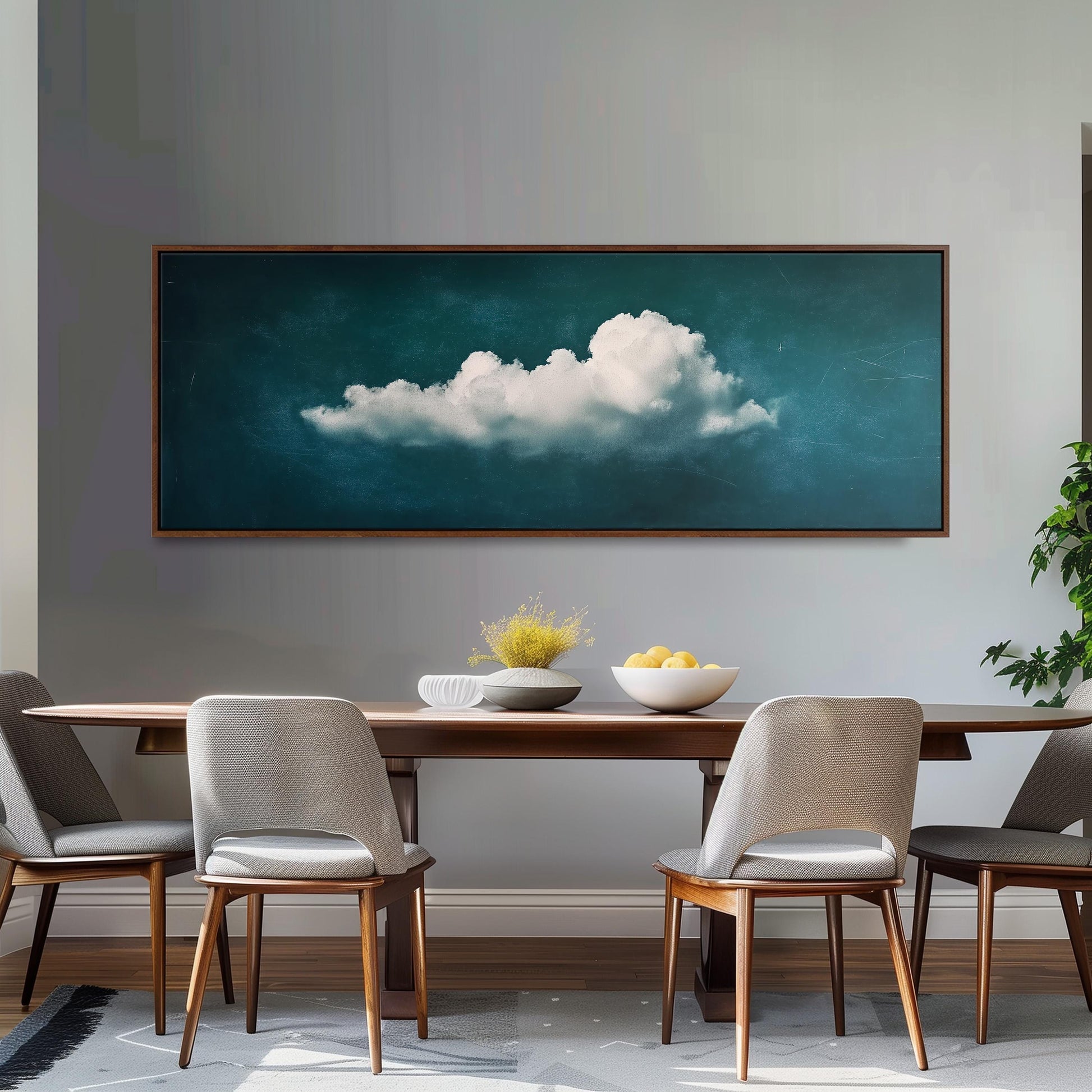 a dining room with a large framed painting of a cloud hanging on the wall above a wooden dining table with four chairs. The table is set with a bowl of fruit and a vase of flowers, creating a cozy and inviting atmosphere.