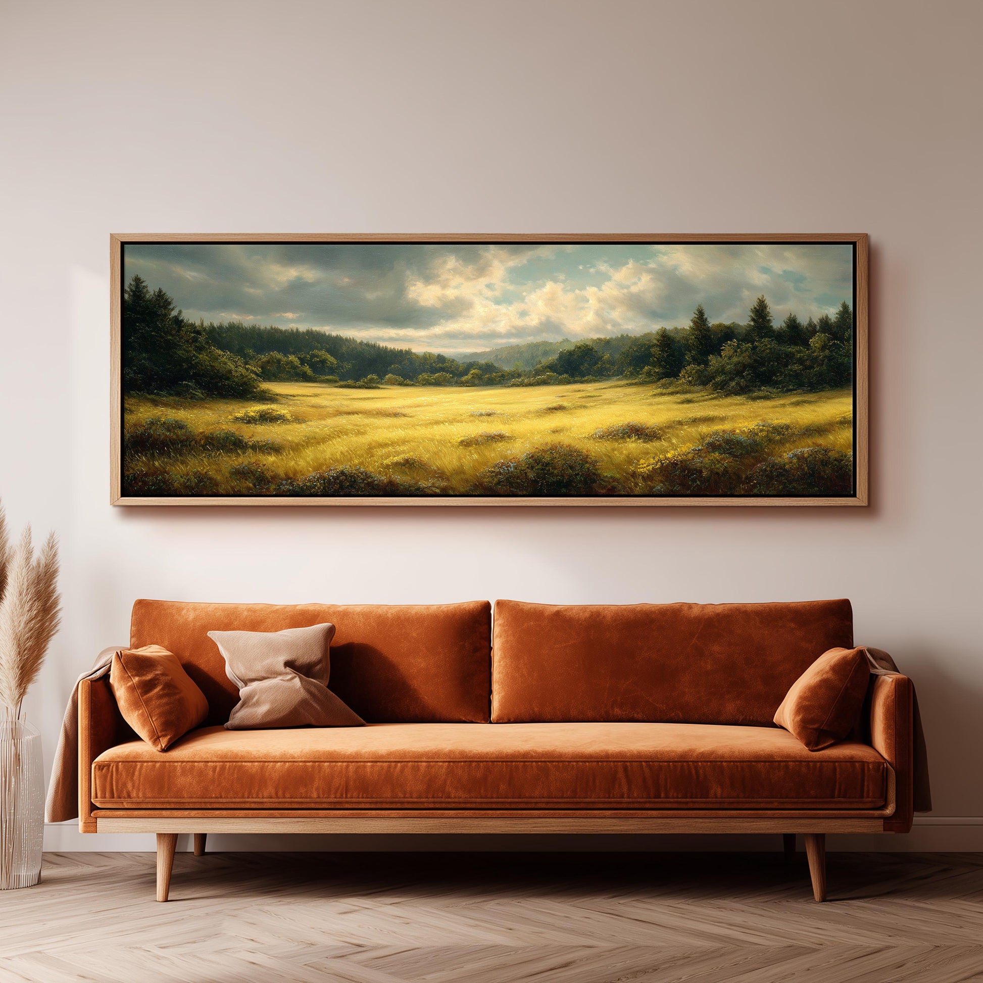 a large landscape painting hanging on a wall above a brown sofa with orange cushions.