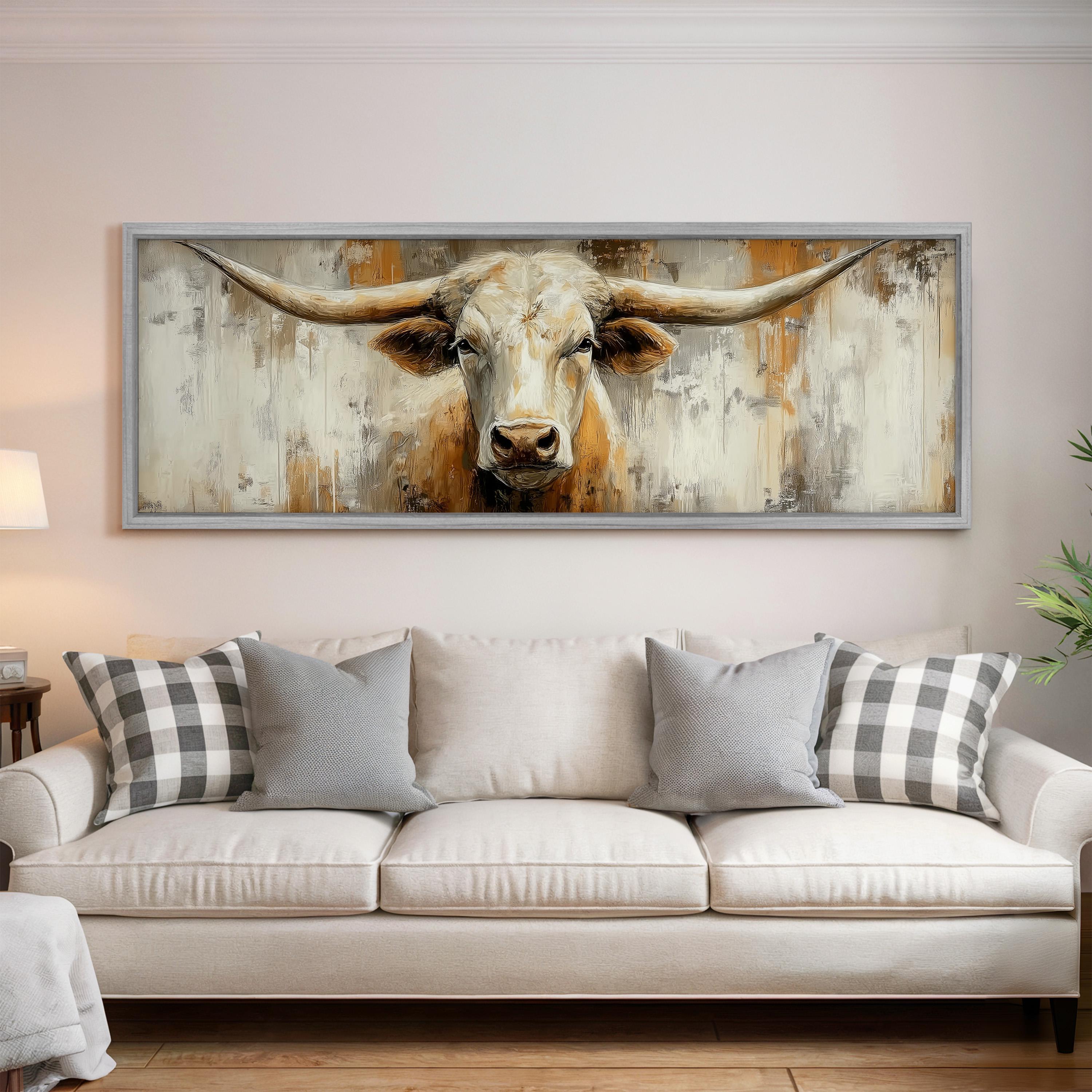 a large painting of a bull's head hanging on a wall above a white couch with gray and white plaid throw pillows.