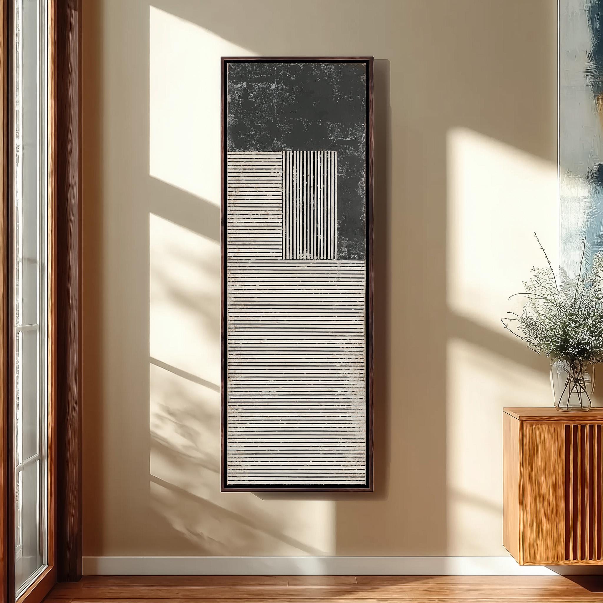 a large abstract painting hanging on a wall, with a wooden cabinet and a vase of flowers placed next to it.