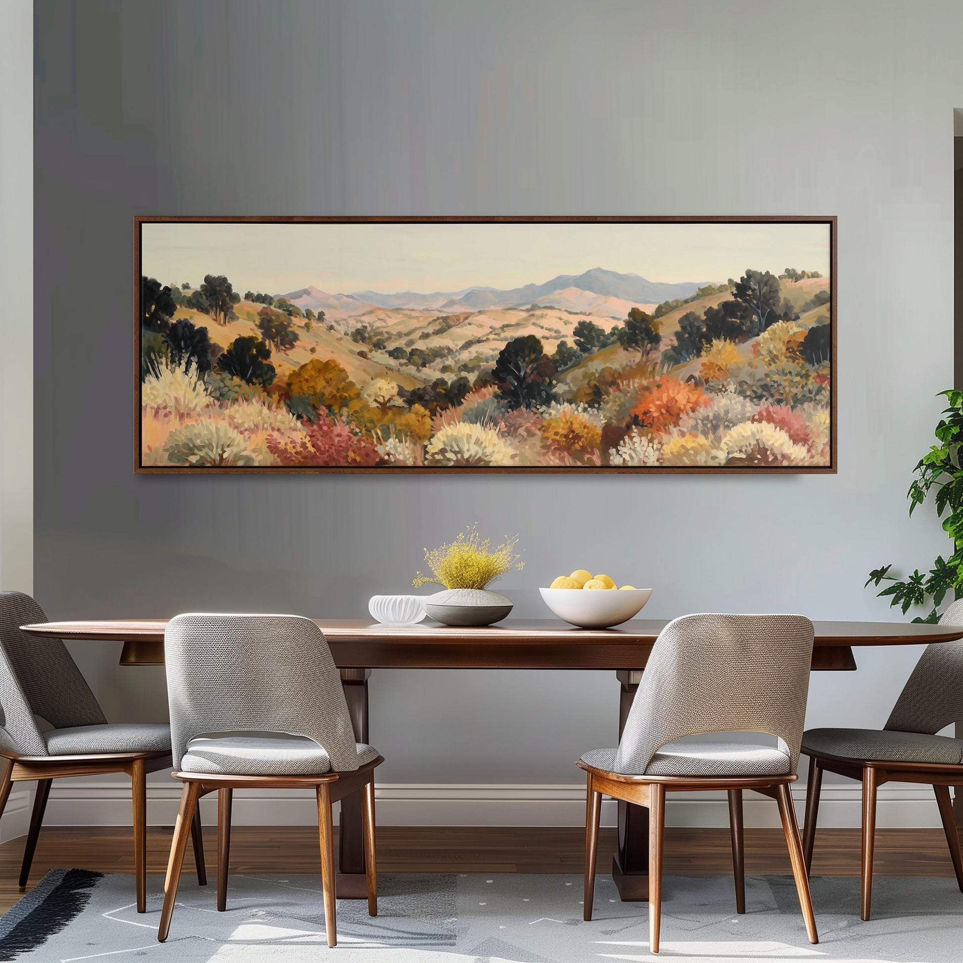 a dining room with a large painting of a countryside landscape hanging on the wall above a wooden dining table with four chairs. The table is set with a bowl of fruit and a vase of flowers, creating a cozy and inviting atmosphere.