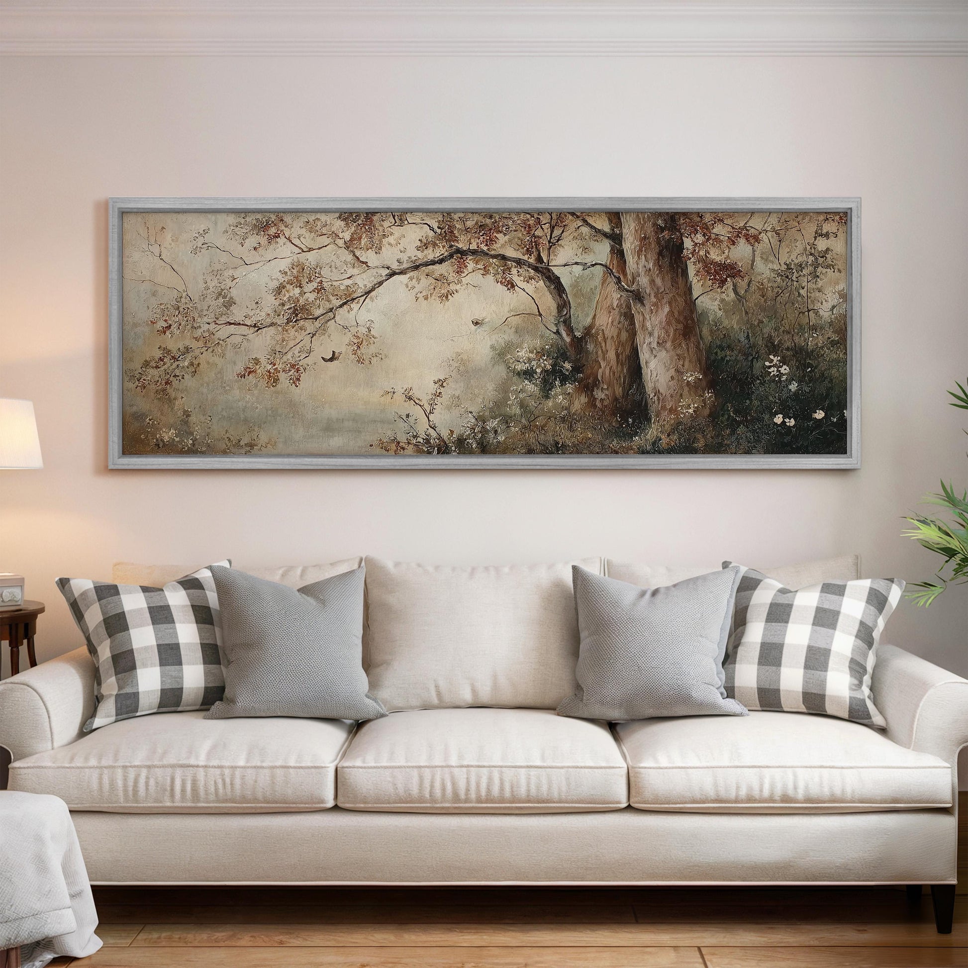 a large, framed painting of a forest scene hanging on a wall above a white sofa with gray and white plaid throw pillows.