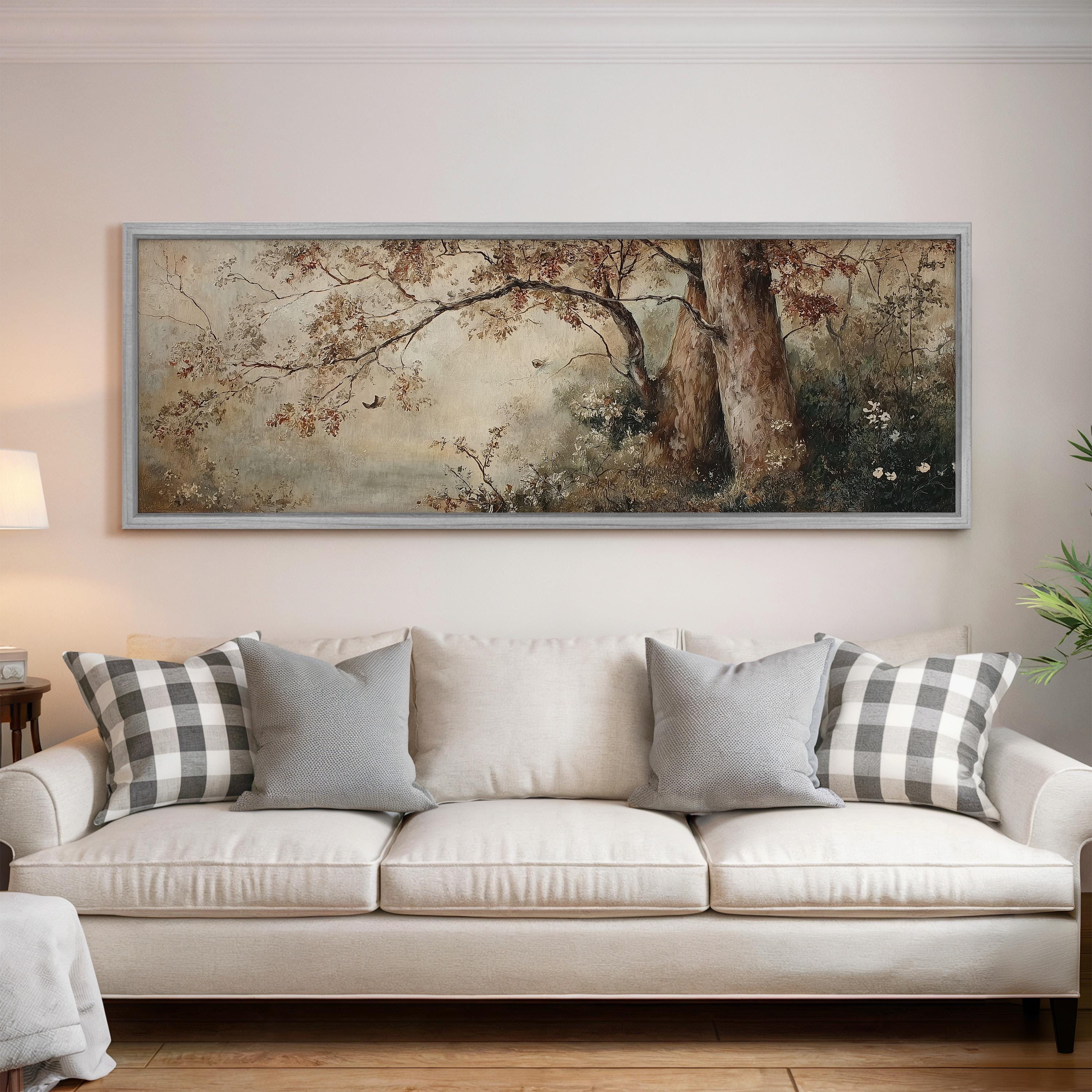 a large, framed painting of a forest scene hanging on a wall above a white sofa with gray and white plaid throw pillows.