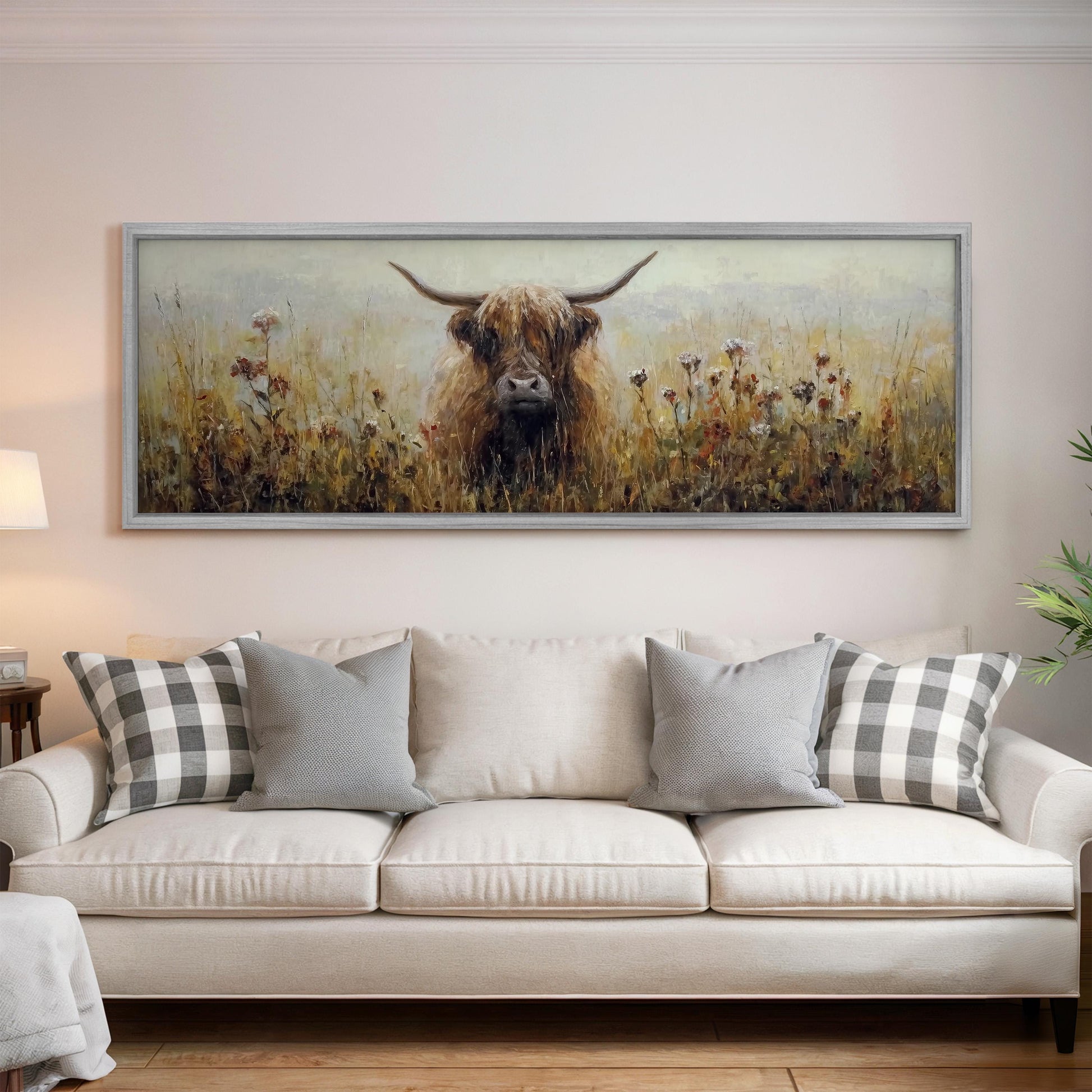a large painting of a cow with horns hanging on a wall above a white couch with pillows.