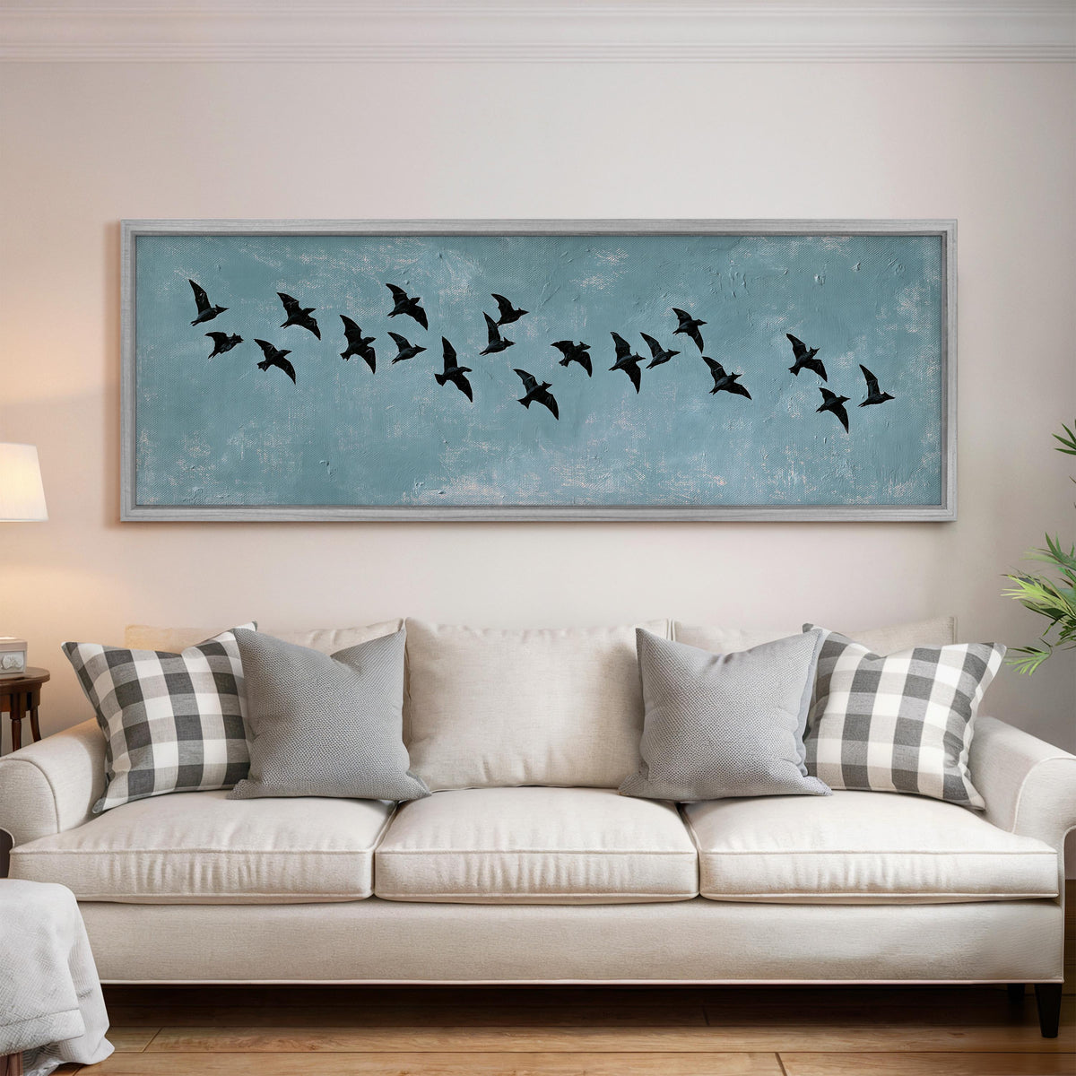 Flock of black birds on a teal sky panoramic canvas print above a white sofa in a bright living room