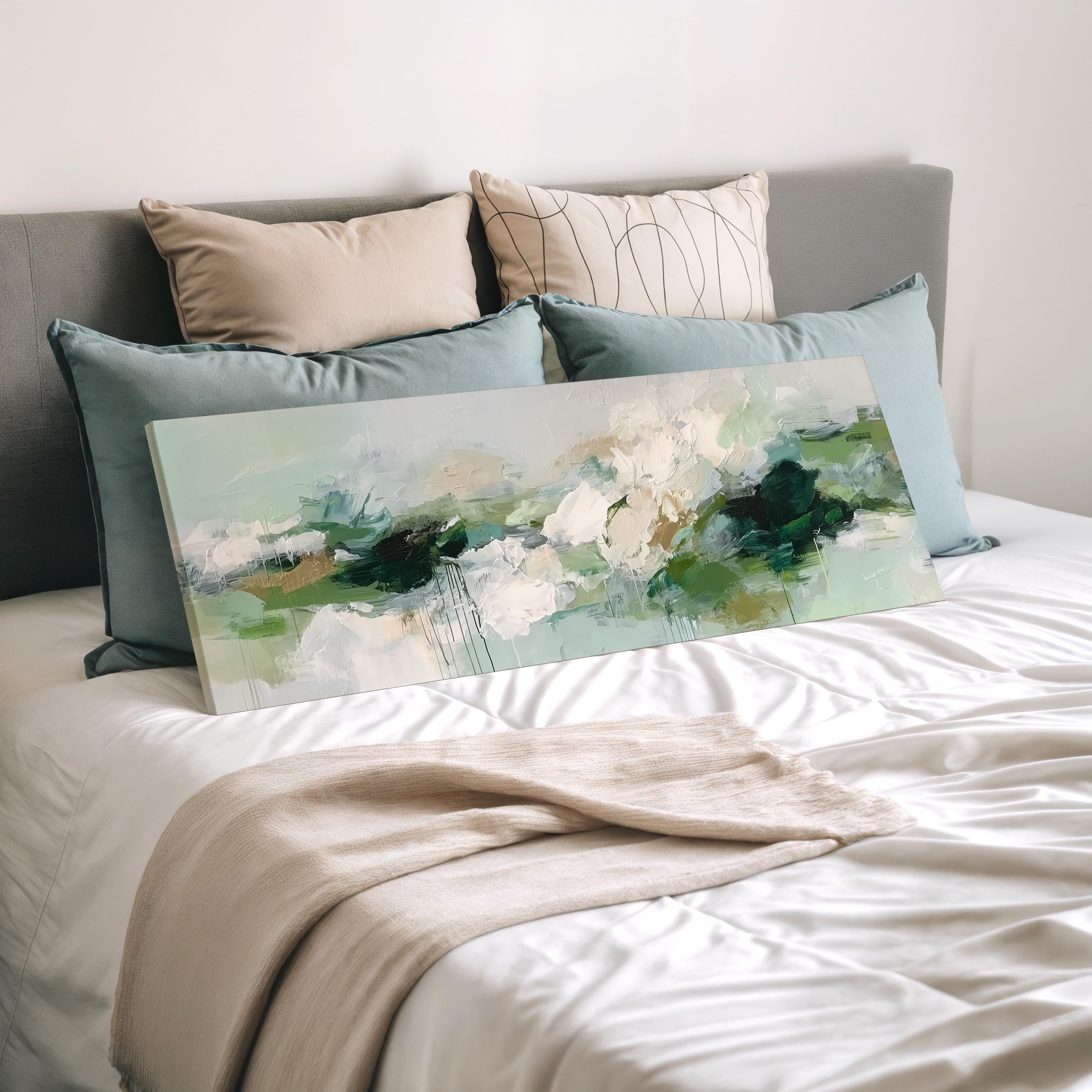 a bedroom with a bed covered in white sheets and a large abstract painting resting on top of the bed.