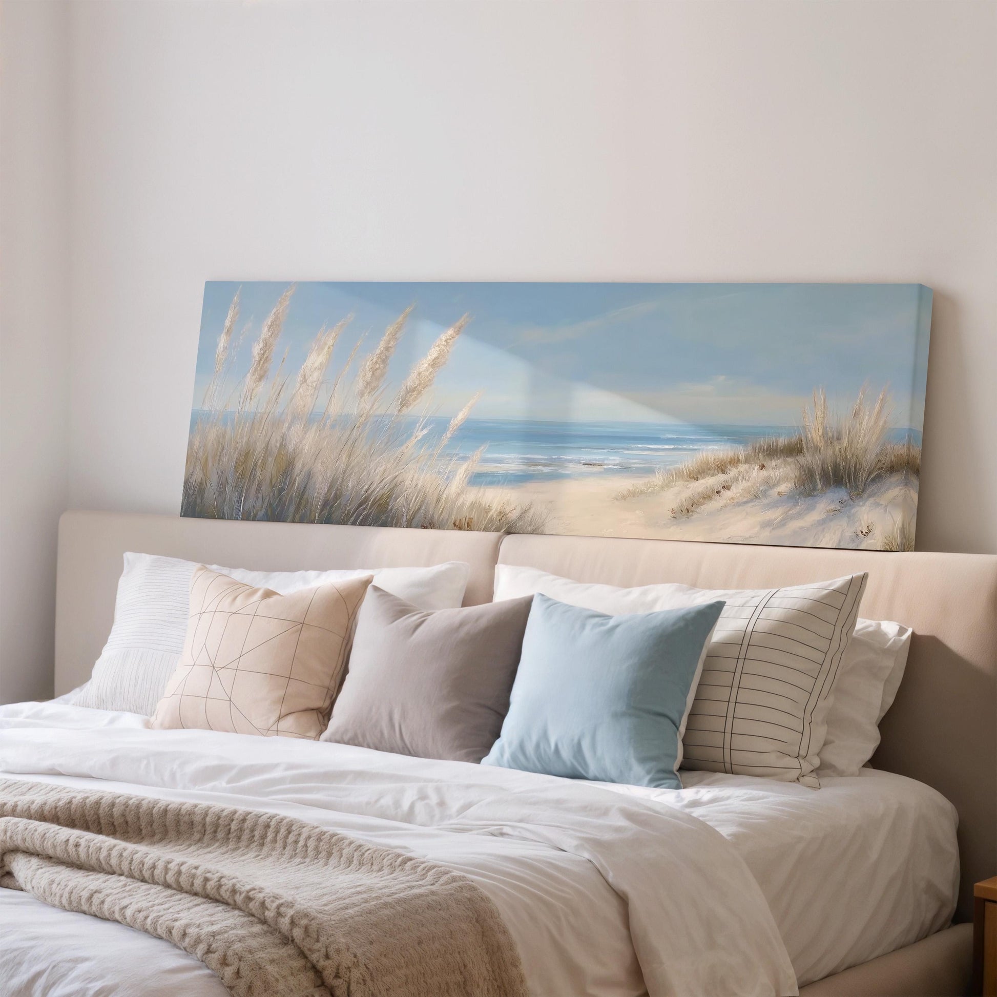 a large painting of a beach scene hanging above a bed with white bedding and pillows.