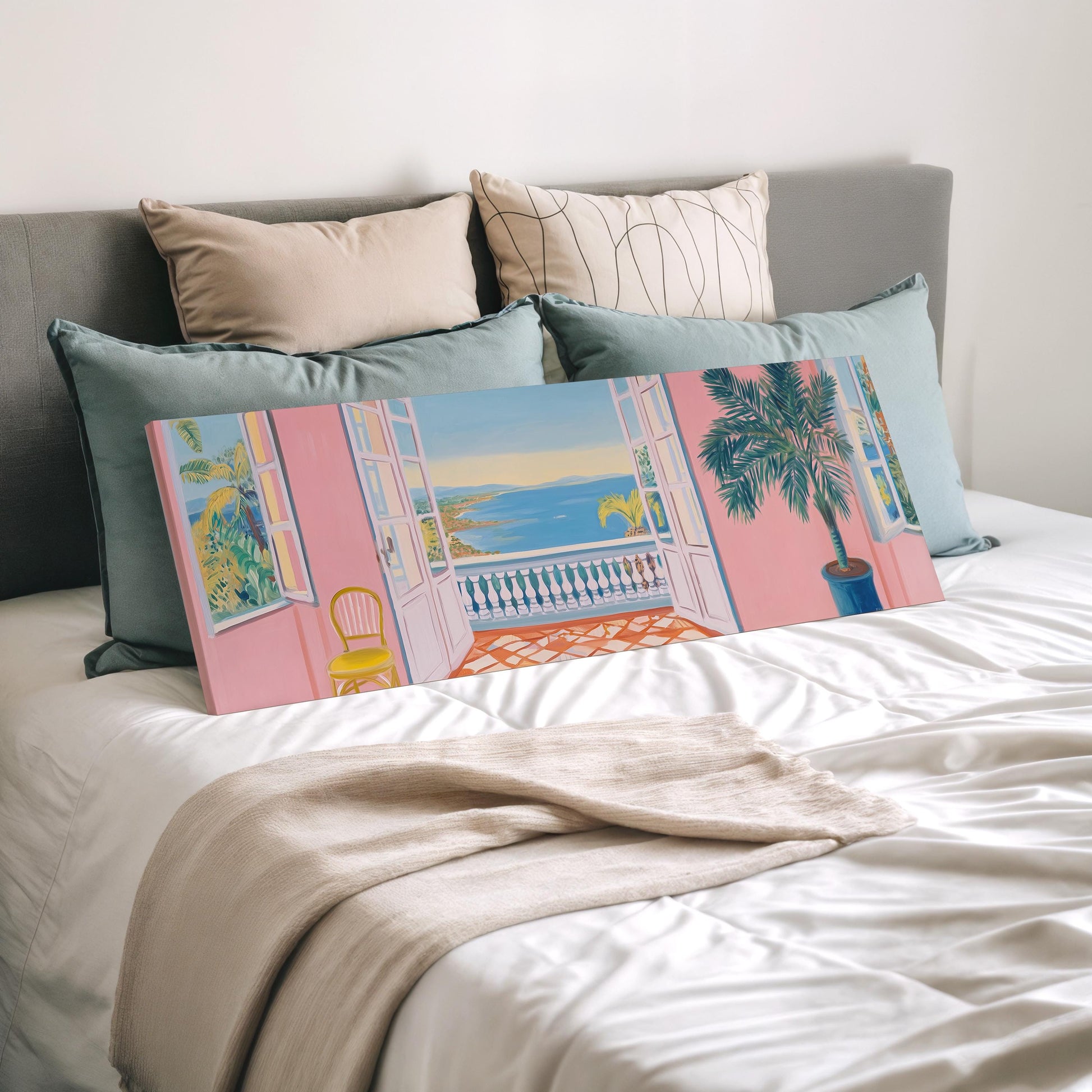 a bedroom with a bed, pillows, and a large canvas print depicting a balcony with a palm tree and a view of the ocean.