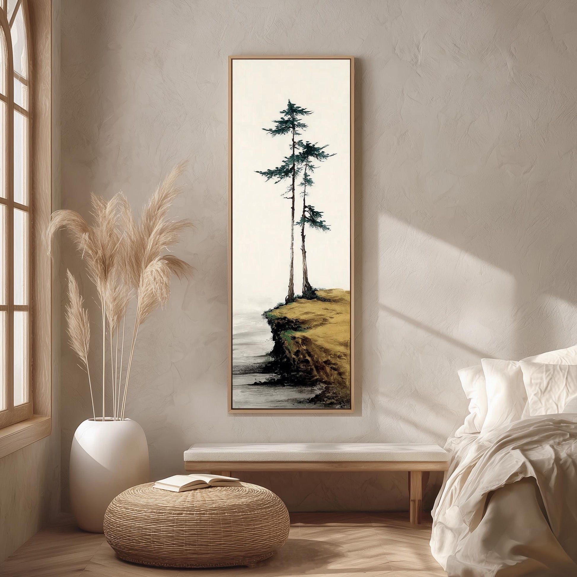 a serene indoor setting with a large painting of a cliff overlooking the ocean hanging on the wall. The painting is framed in a white frame and is surrounded by a beige vase filled with tall, light-colored reeds. The room also includes a bed, a bench, and a woven ottoman, creating a cozy and inviting atmosphere.