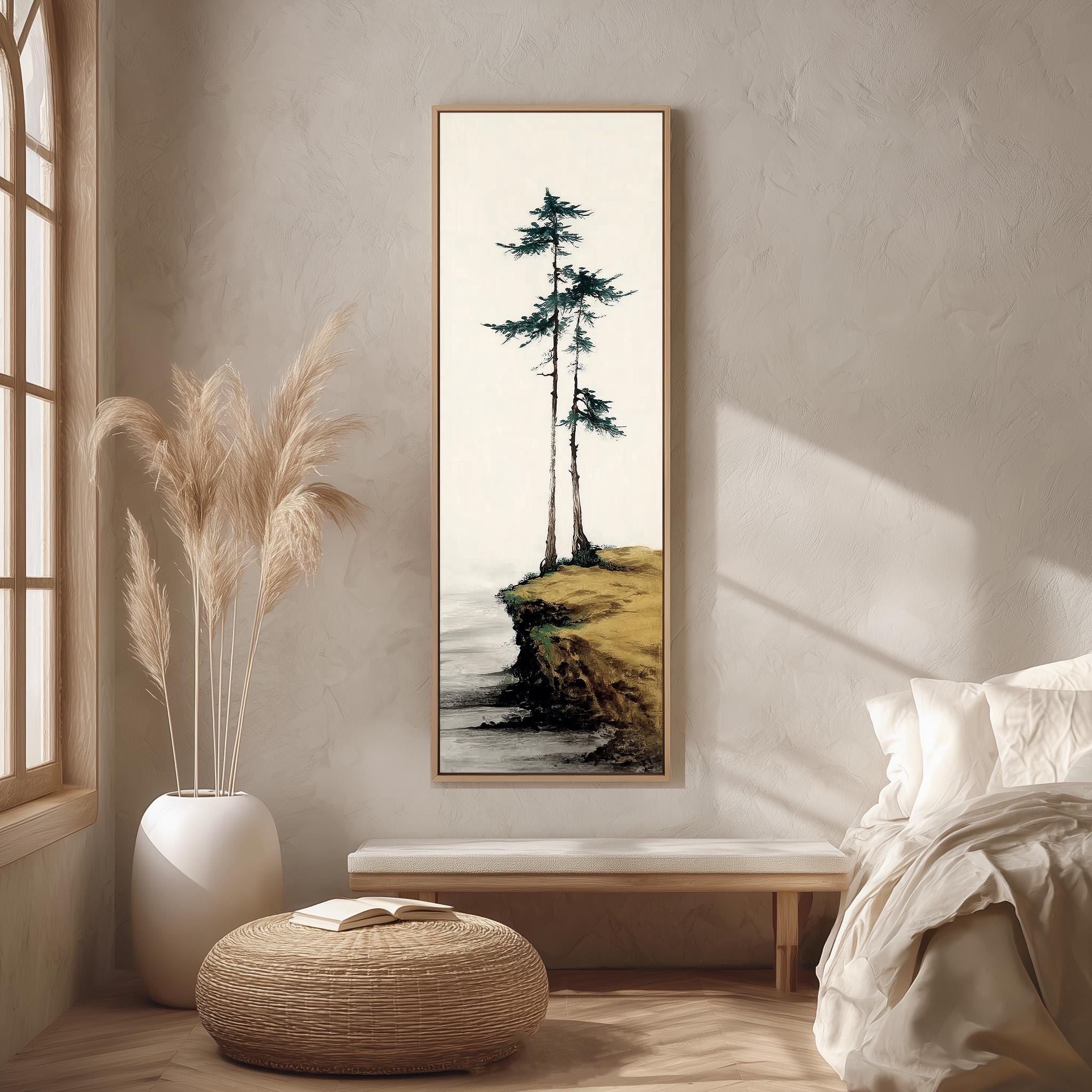 a serene indoor setting with a large painting of a cliff overlooking the ocean hanging on the wall. The painting is framed in a white frame and is surrounded by a beige vase filled with tall, light-colored reeds. The room also includes a bed, a bench, and a woven ottoman, creating a cozy and inviting atmosphere.