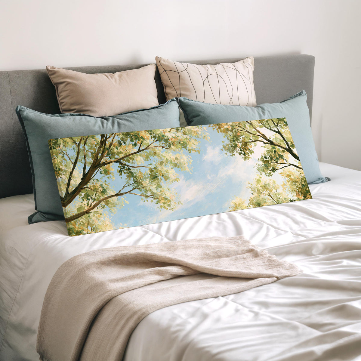 Sunlit leafy branches framing soft clouds wide panoramic canvas print laid on a bed to show its size