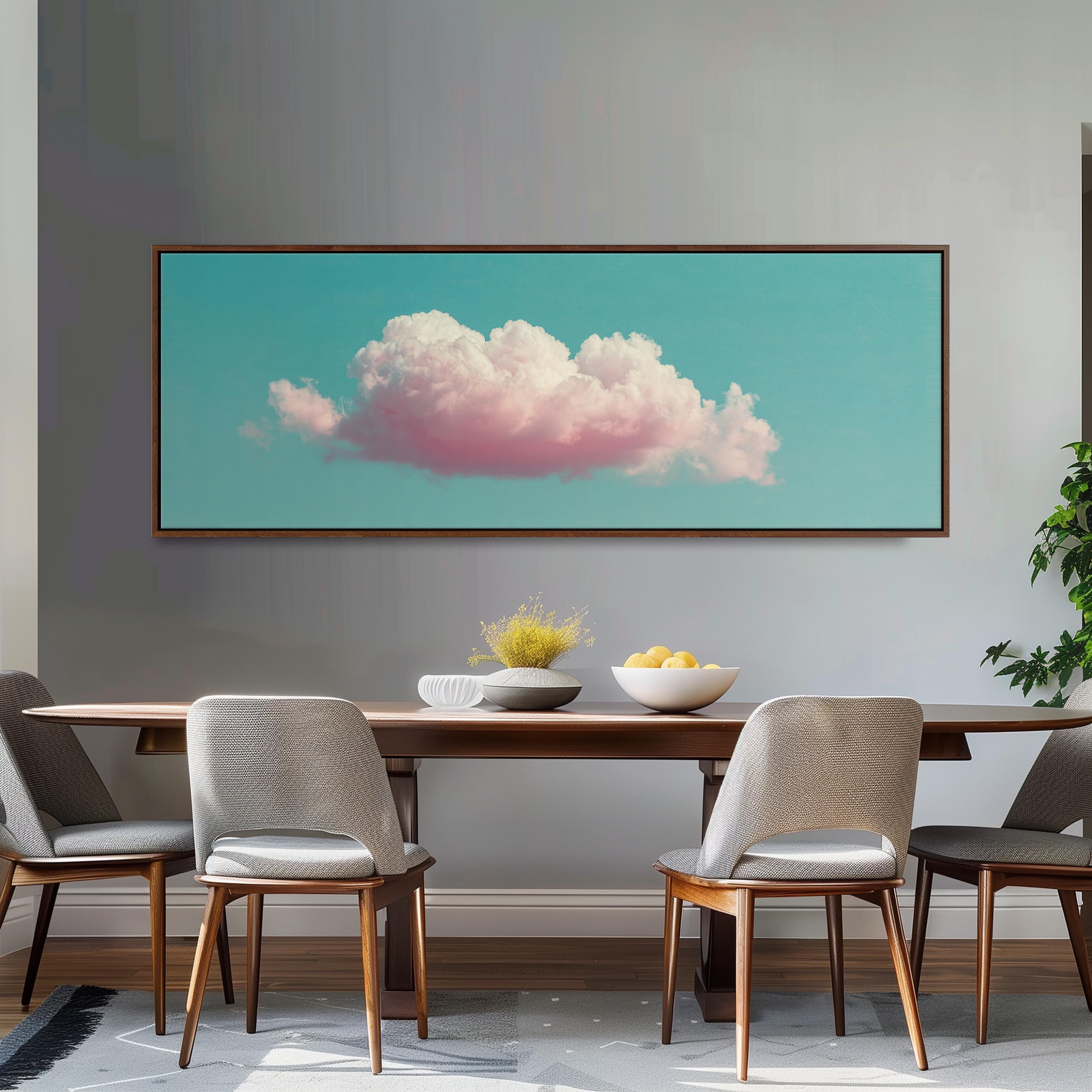a dining room with a wooden table and four chairs. Above the table, there is a large framed picture of a cloud with pink and white colors. The table is set with a bowl of fruit and a vase of flowers.