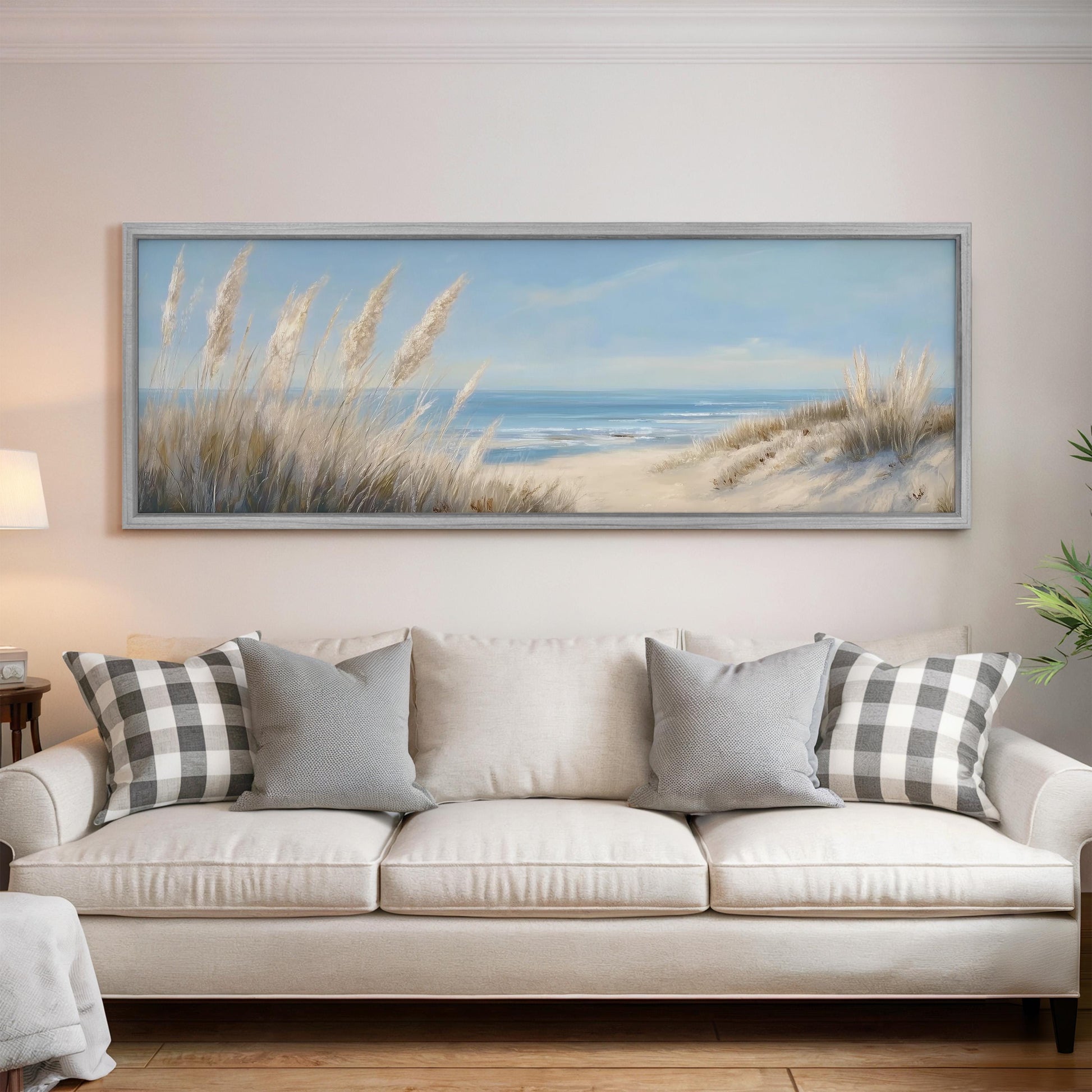 a large painting of a beach scene hanging on a wall above a white sofa with gray and white patterned pillows.