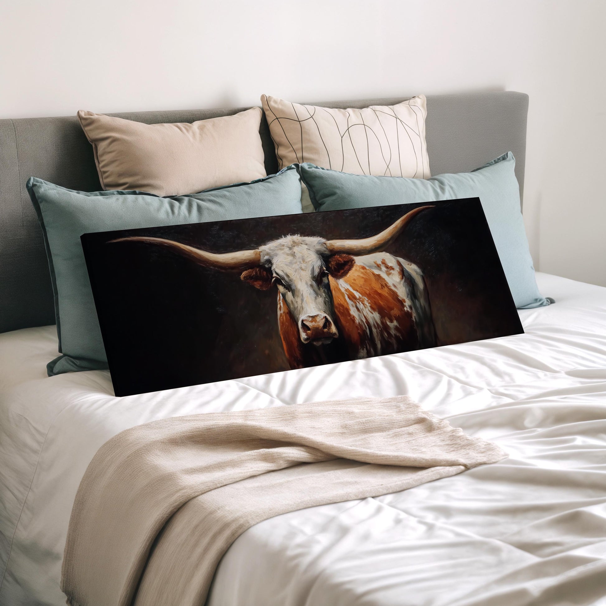 a large canvas print of a bull with long horns, displayed on a bed with a white comforter and pillows.