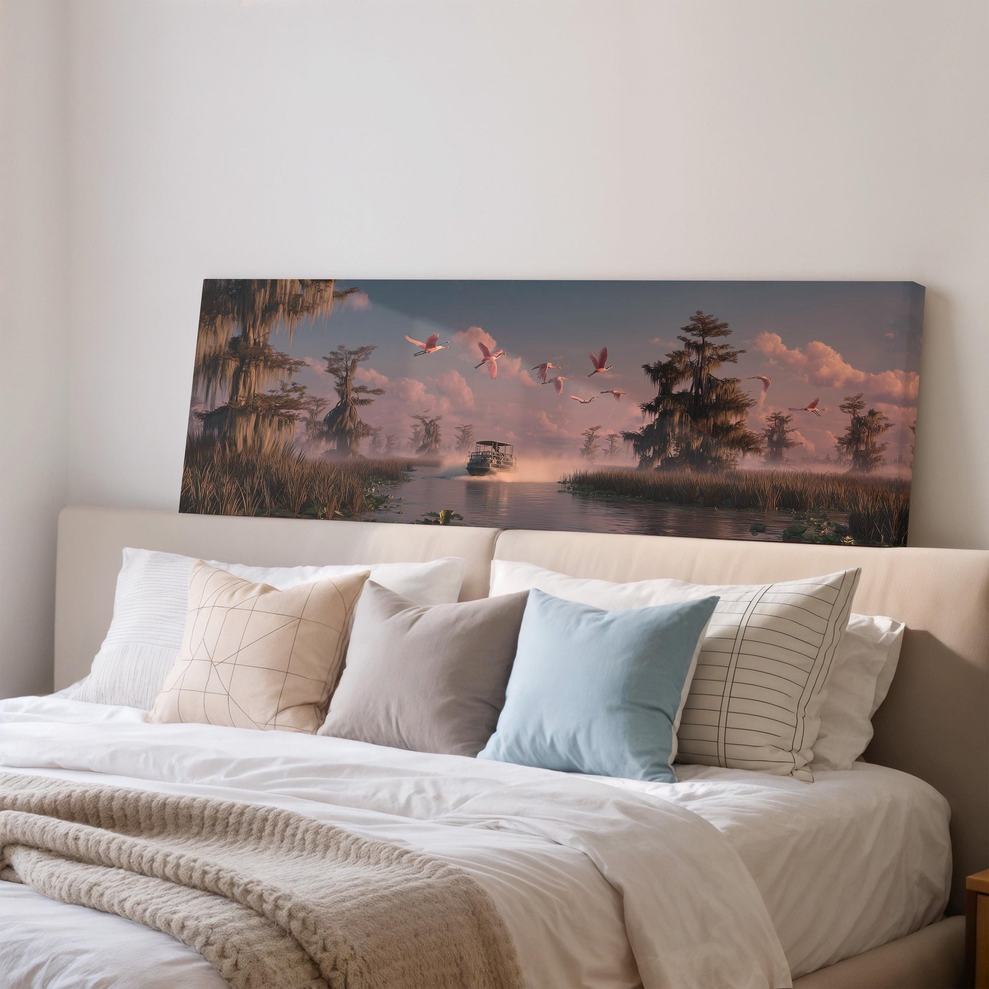 a large painting of a serene landscape with a river, trees, and birds in flight, hanging above a bed with white pillows and a gray blanket.