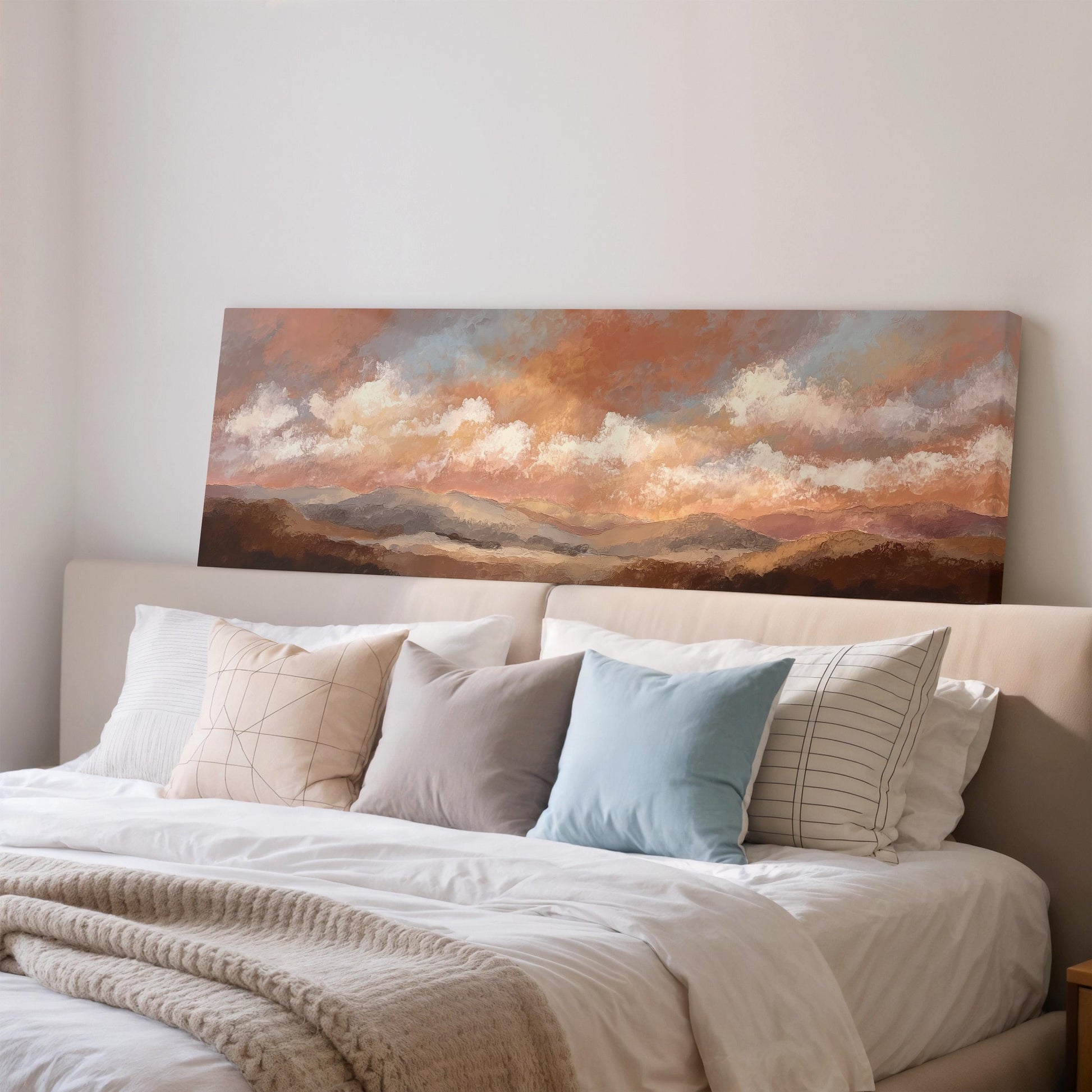 a large painting of a landscape hanging on a wall above a bed with white pillows and a gray blanket.