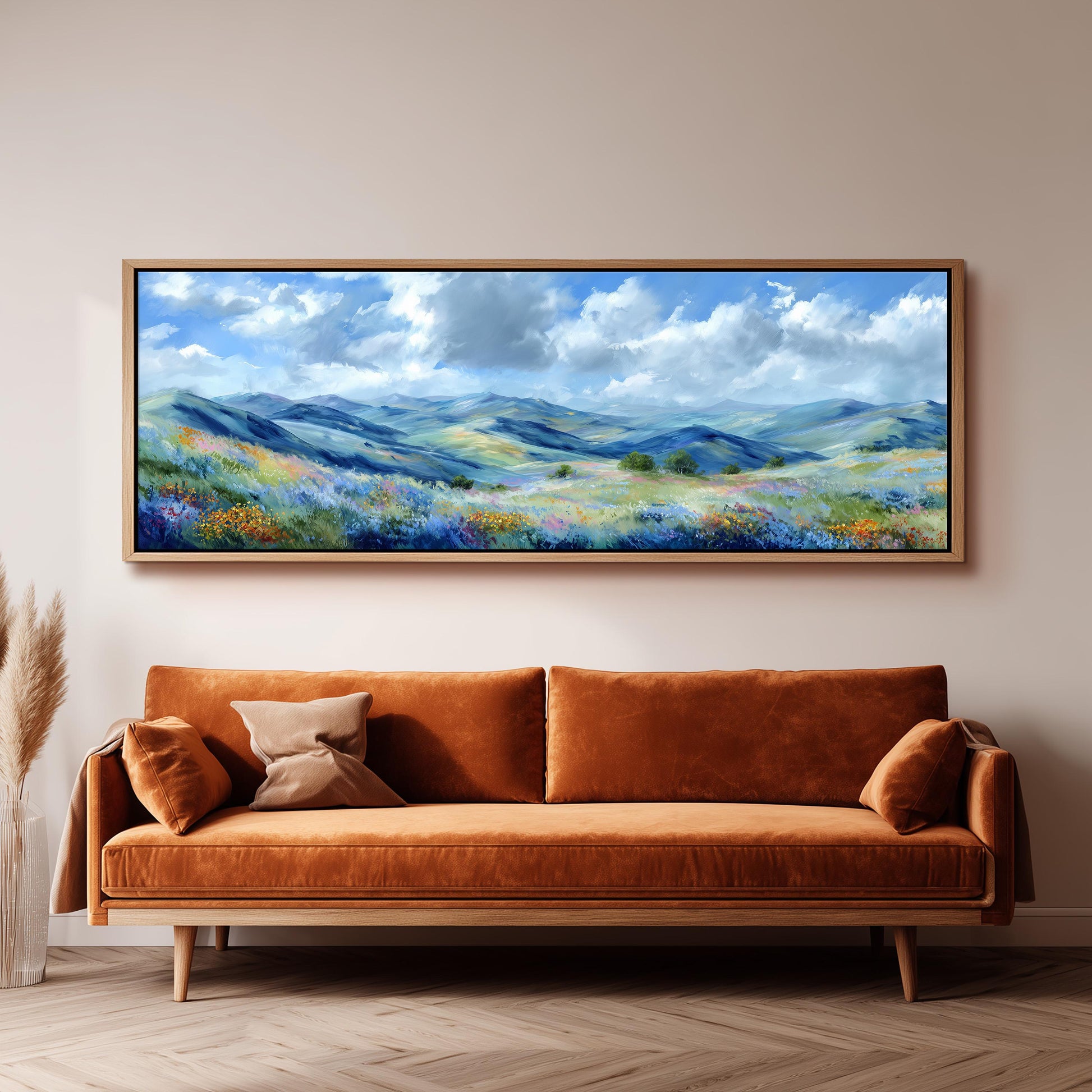 a large, framed painting of a mountainous landscape with a blue sky and fluffy clouds, hanging on a wall above a brown sofa.