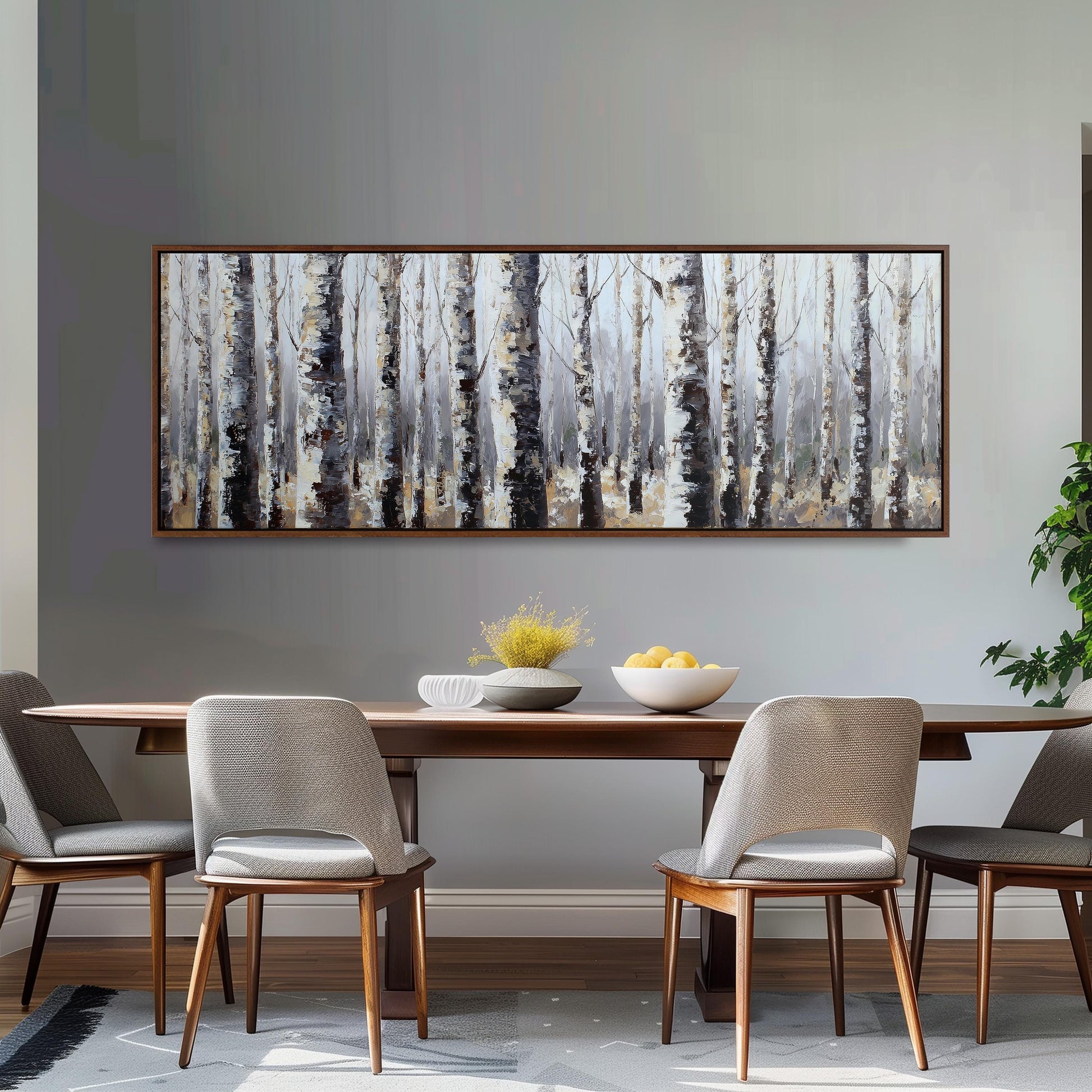 a dining room with a large painting of a forest scene hanging on the wall above a wooden dining table with four chairs. The table is set with a bowl of fruit and a vase of flowers, creating a cozy and inviting atmosphere.