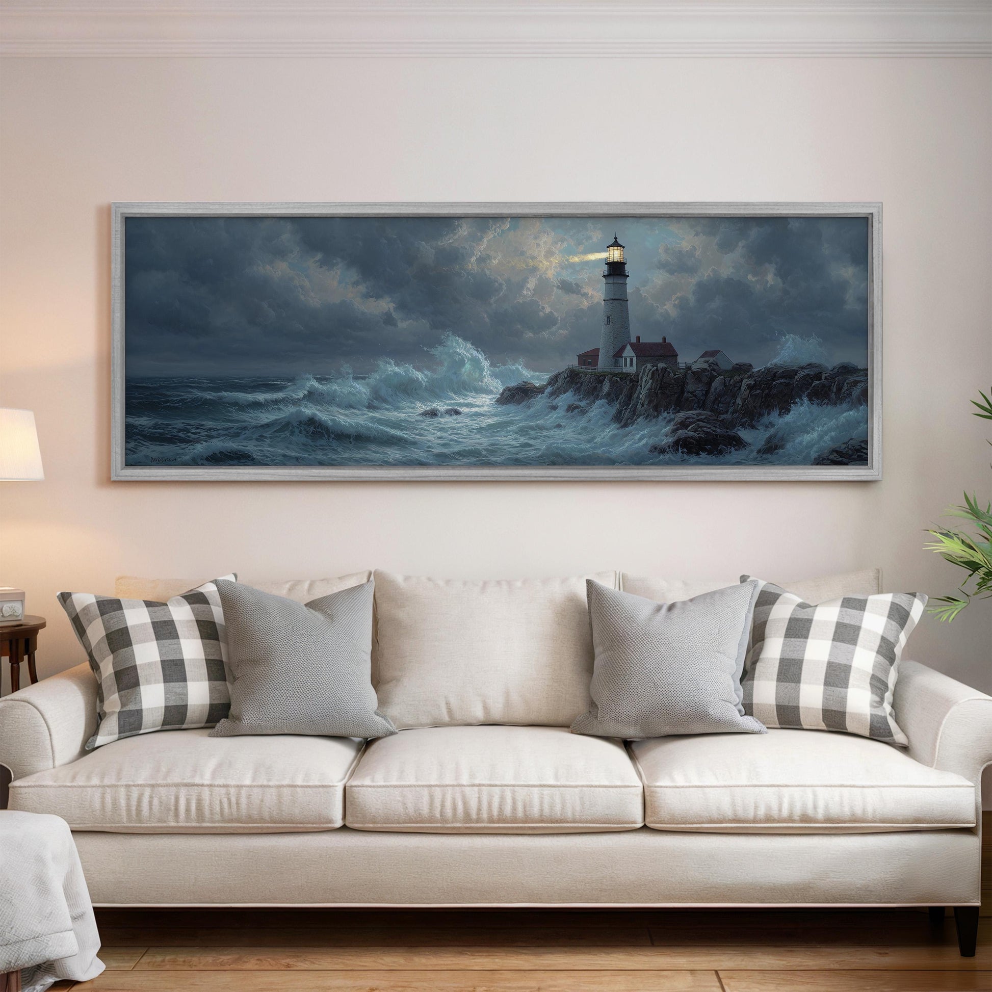 a large painting of a lighthouse on a rocky shore, hanging on a wall above a white sofa with patterned throw pillows.