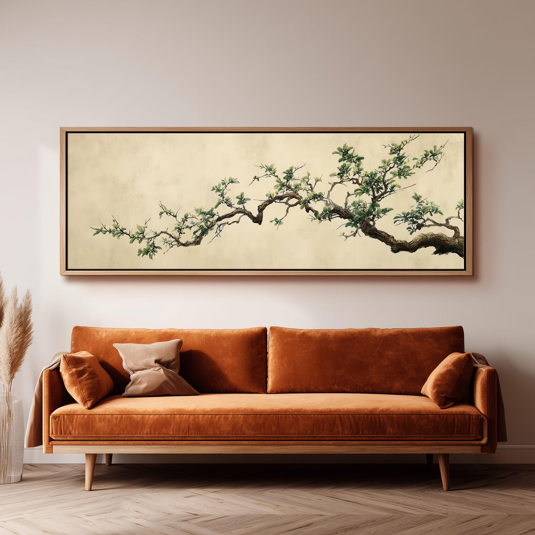 a large, framed painting of a tree branch with green leaves hanging above a brown sofa in a living room setting.
