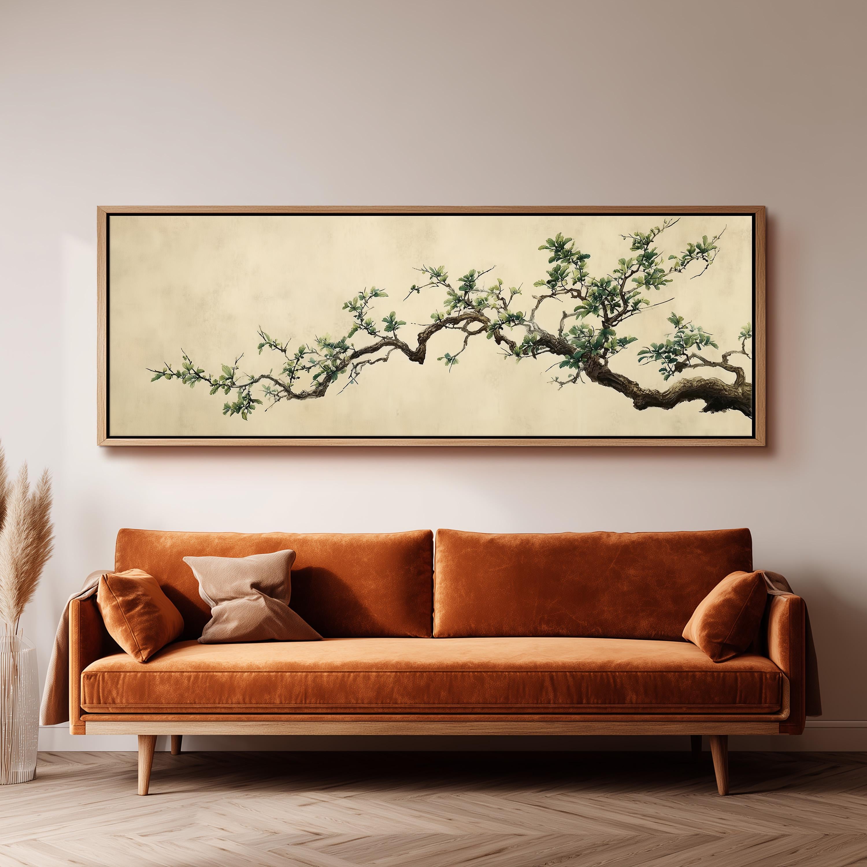a large, framed painting of a tree branch with green leaves hanging above a brown sofa in a living room setting.