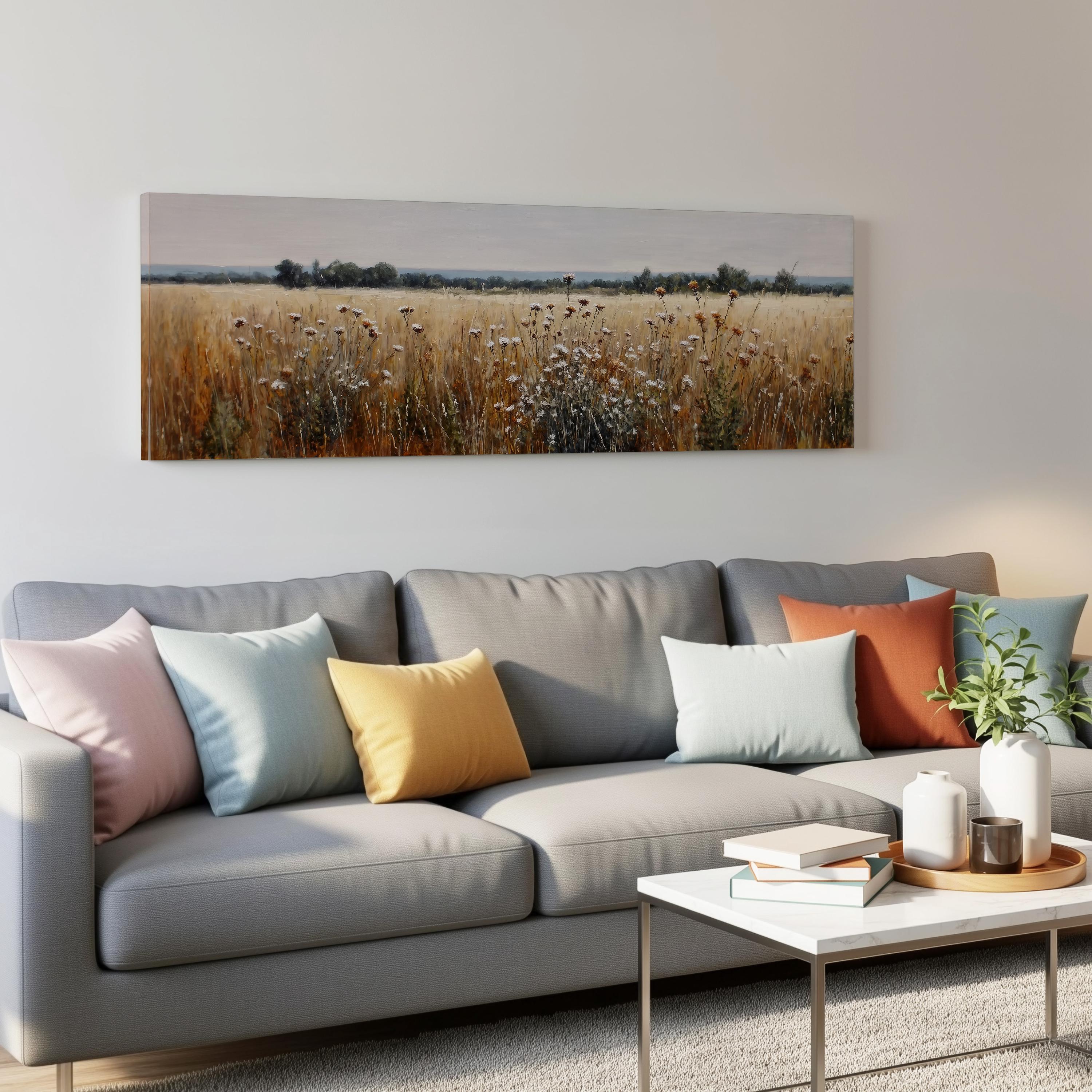 a living room with a gray sofa adorned with colorful throw pillows, a coffee table with books and a plant, and a large landscape painting hanging on the wall above the sofa.