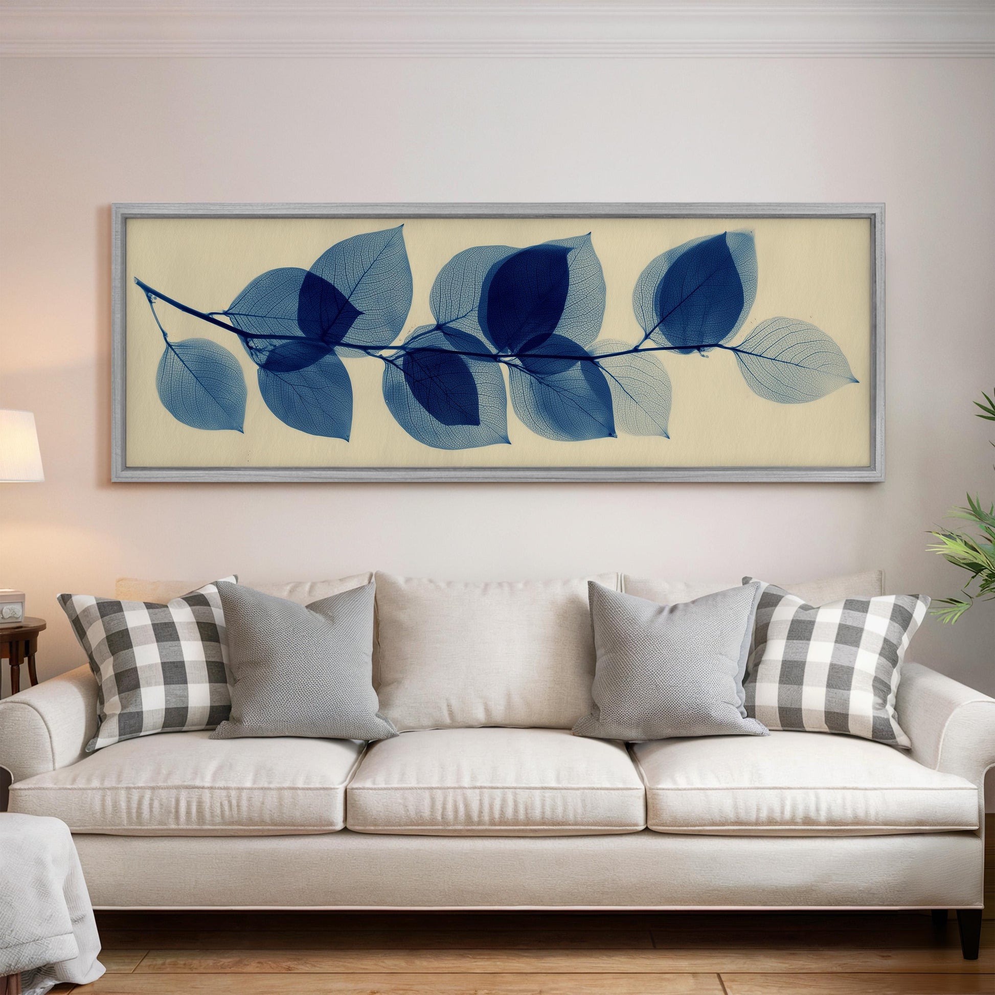 a large framed artwork of blue leaves hanging on a wall above a white couch with gray and white pillows.