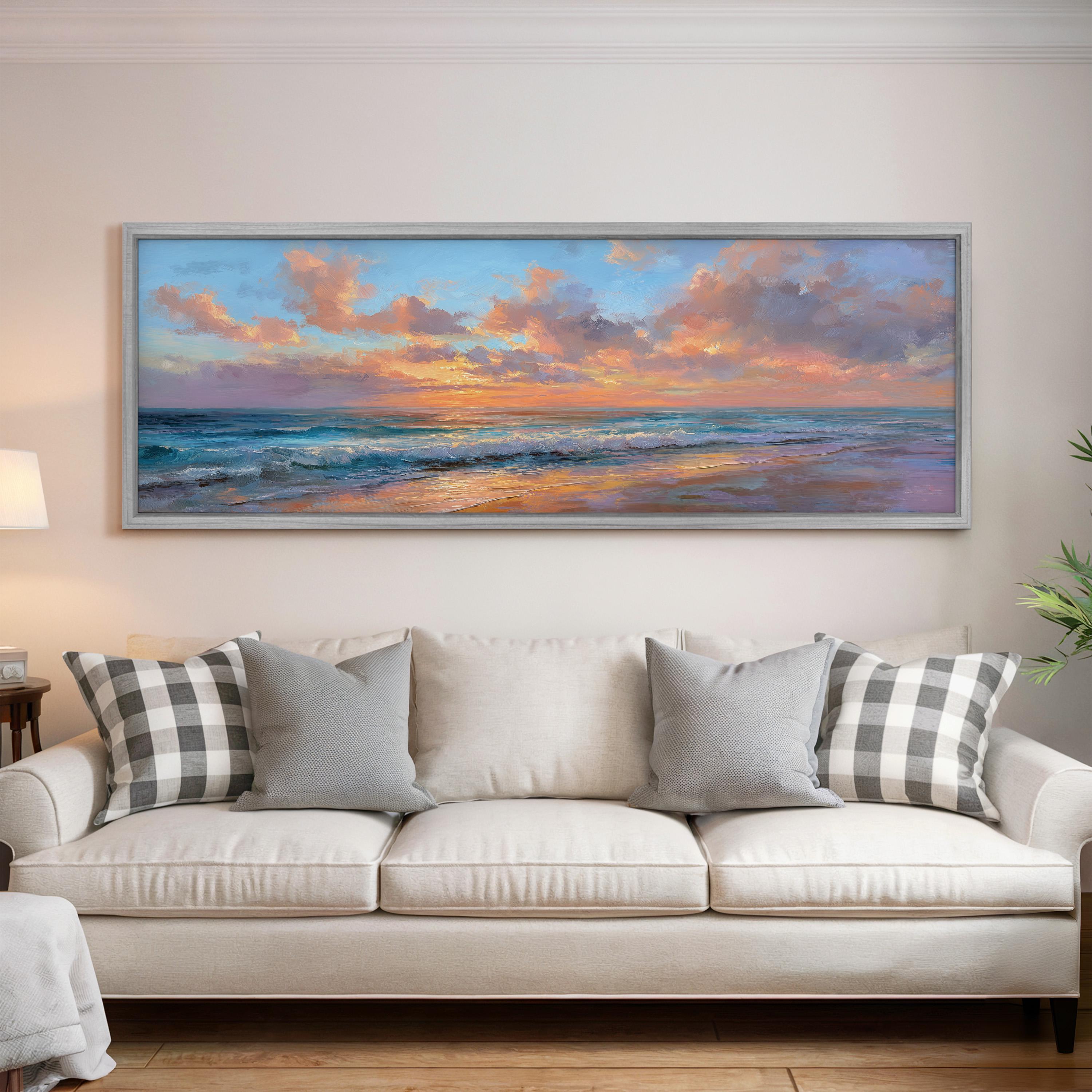 a large, framed painting of a serene beach scene hanging on a wall above a white sofa with gray and white patterned pillows.