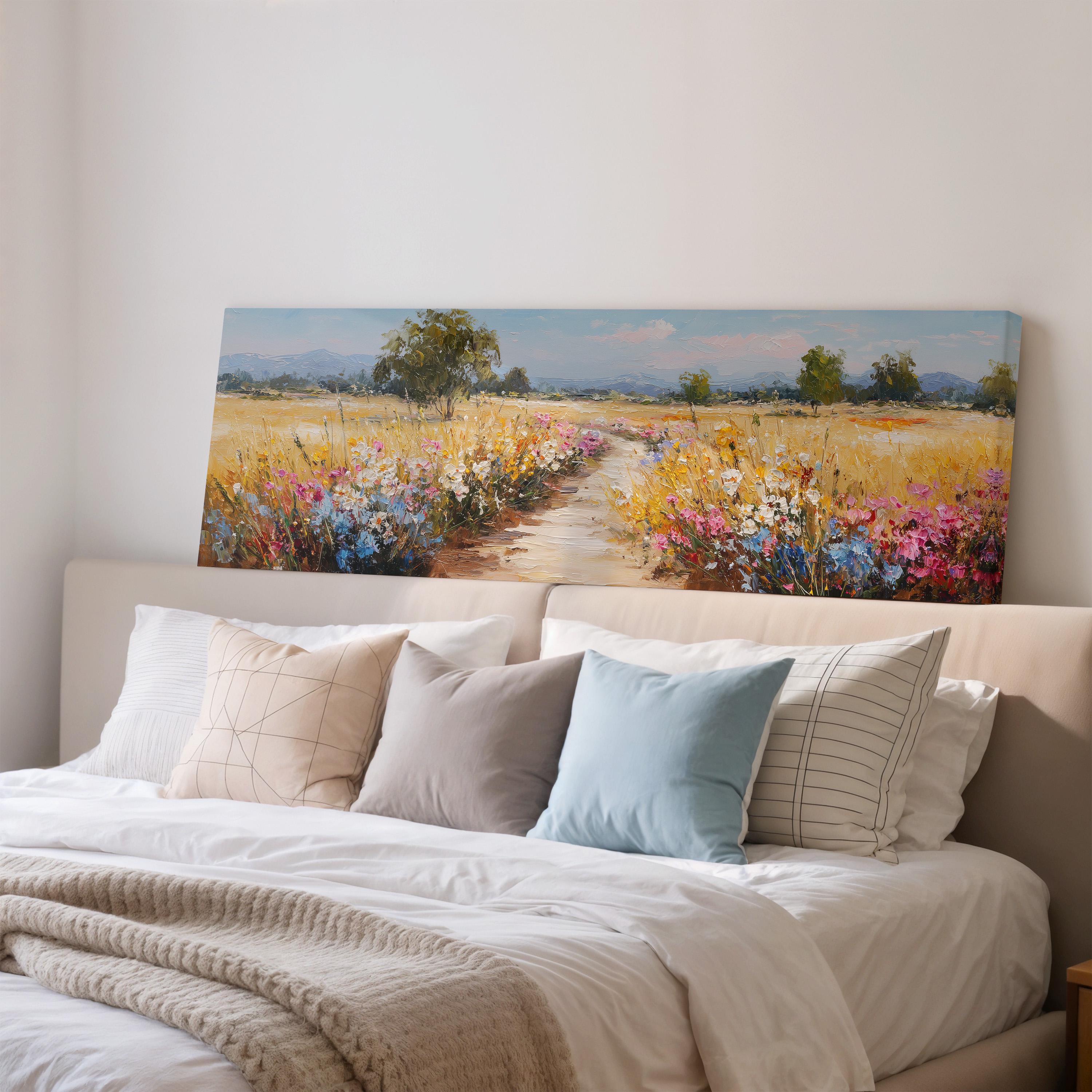 a large painting of a field with flowers hanging above a bed with white sheets and pillows.