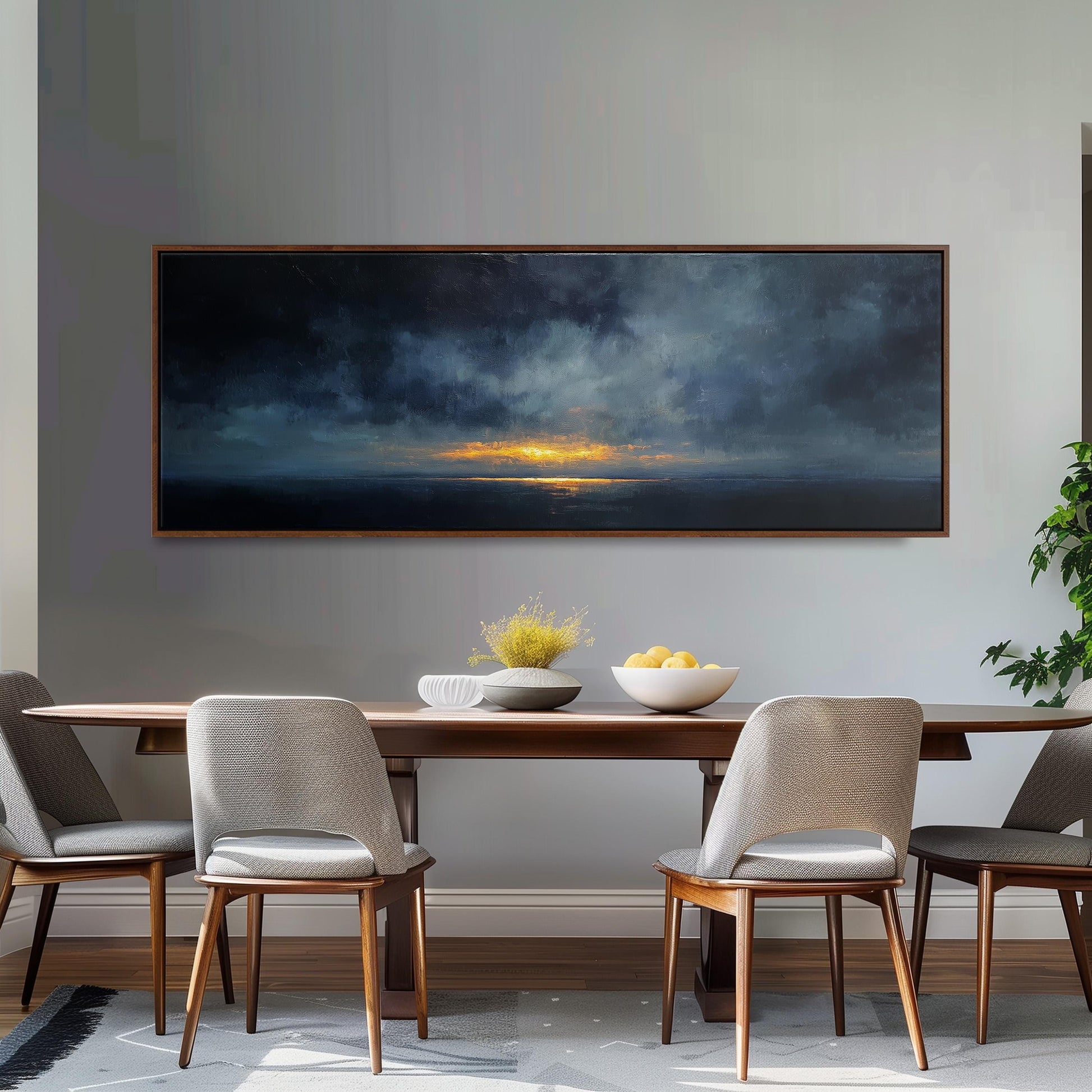 a dining room with a large painting of a sunset over the ocean hanging on the wall above a wooden dining table with four chairs. The table is set with a bowl of fruit and a vase of flowers, creating a cozy and inviting atmosphere.
